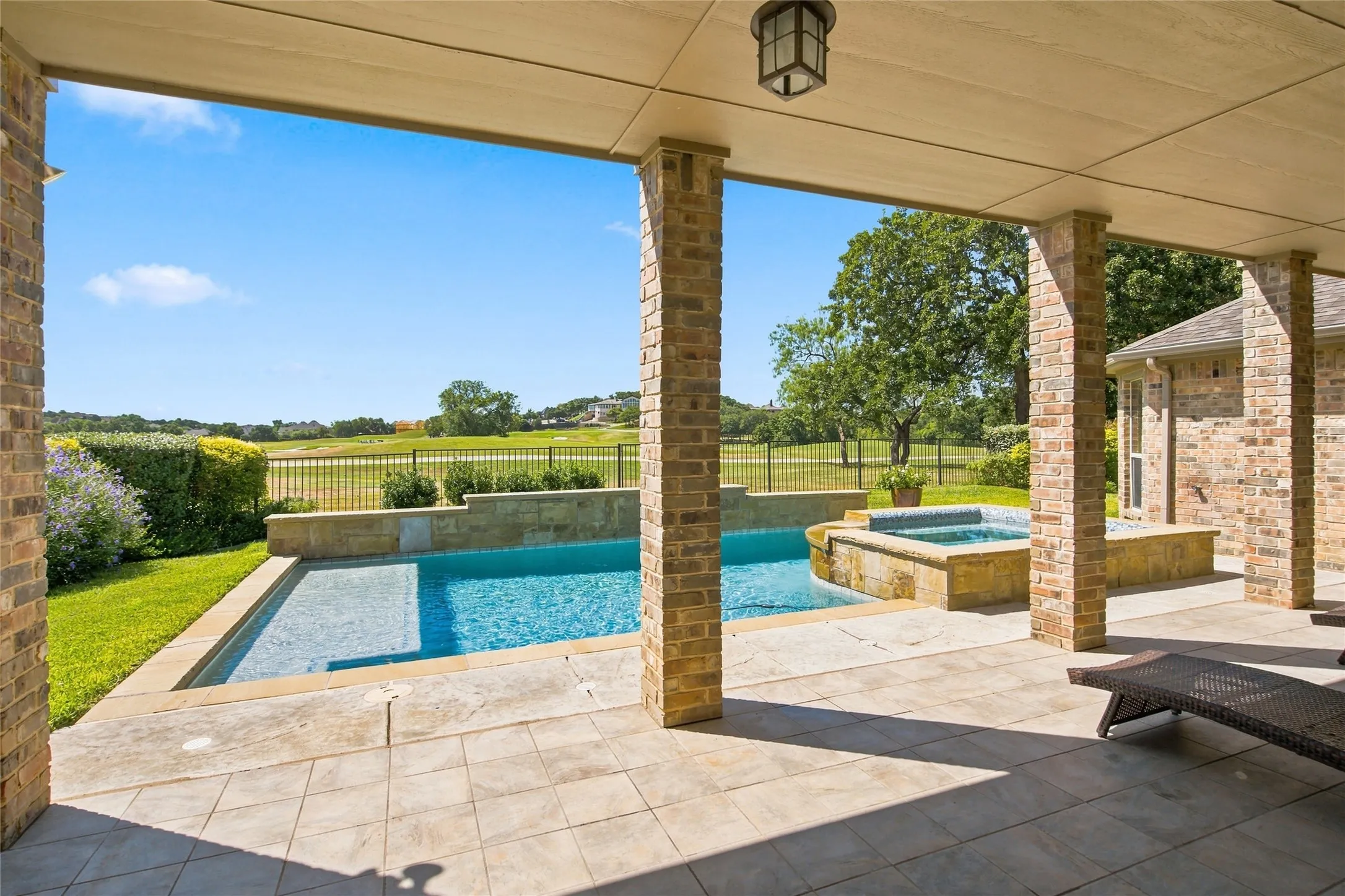 Large covered patio overlooking 15th hole on the golf course with a stone tile surface, brick columns, swimming pool and spa.