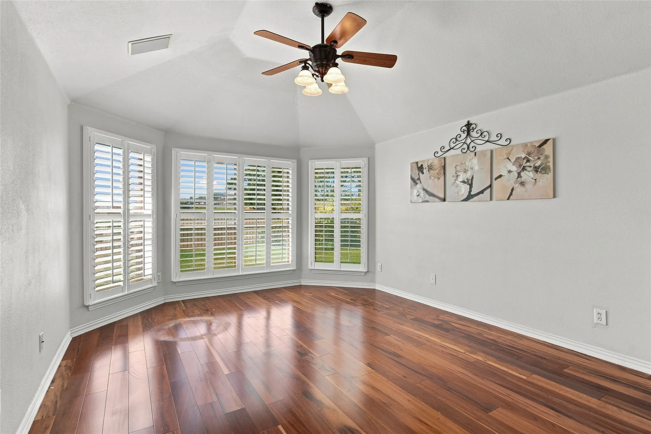 Primary bedroom with bay window with plantation shutters, vaulted ceiling, wood-finish flooring, and a ceiling fan with integrated lighting