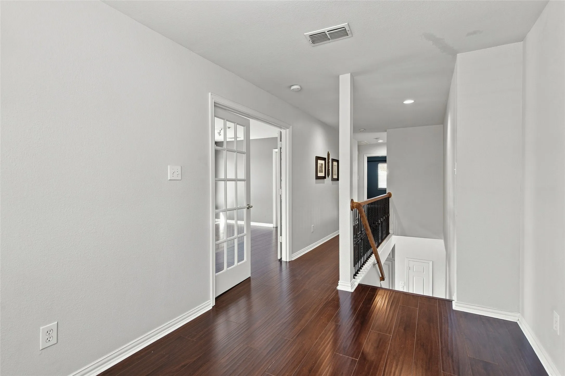 Bright upper level featuring durable wood plank laminate flooring throughout, white trim, recessed lighting, and a staircase with a dark wrought iron and wood banister.