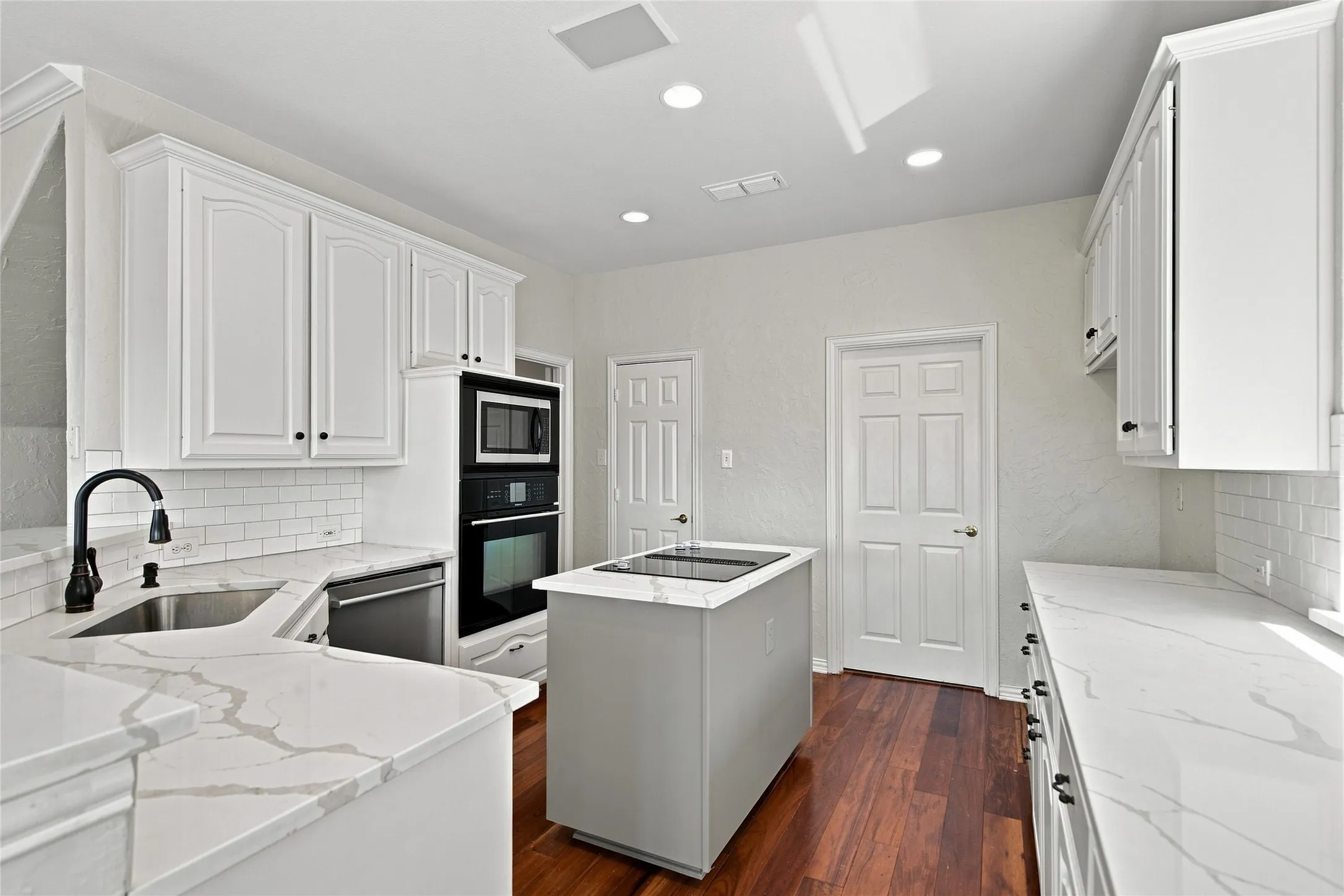 White cabinetry, quartz countertops, subway tile backsplash, stainless steel appliances, and a central island with a cooktop.