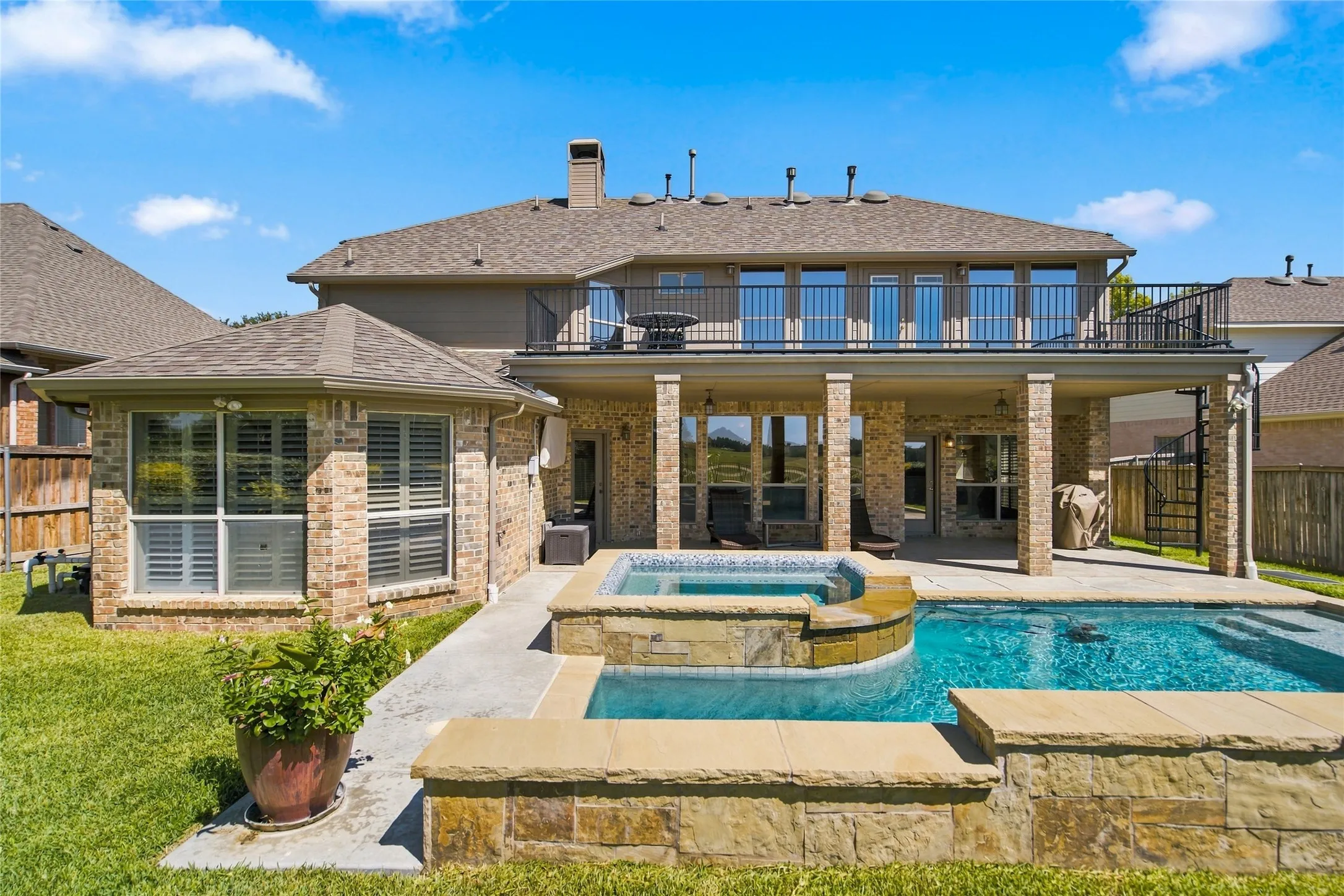 Expansive brick exterior with a second-story balcony, a covered patio, a built-in swimming pool, staircase to balcony and an integrated spa.