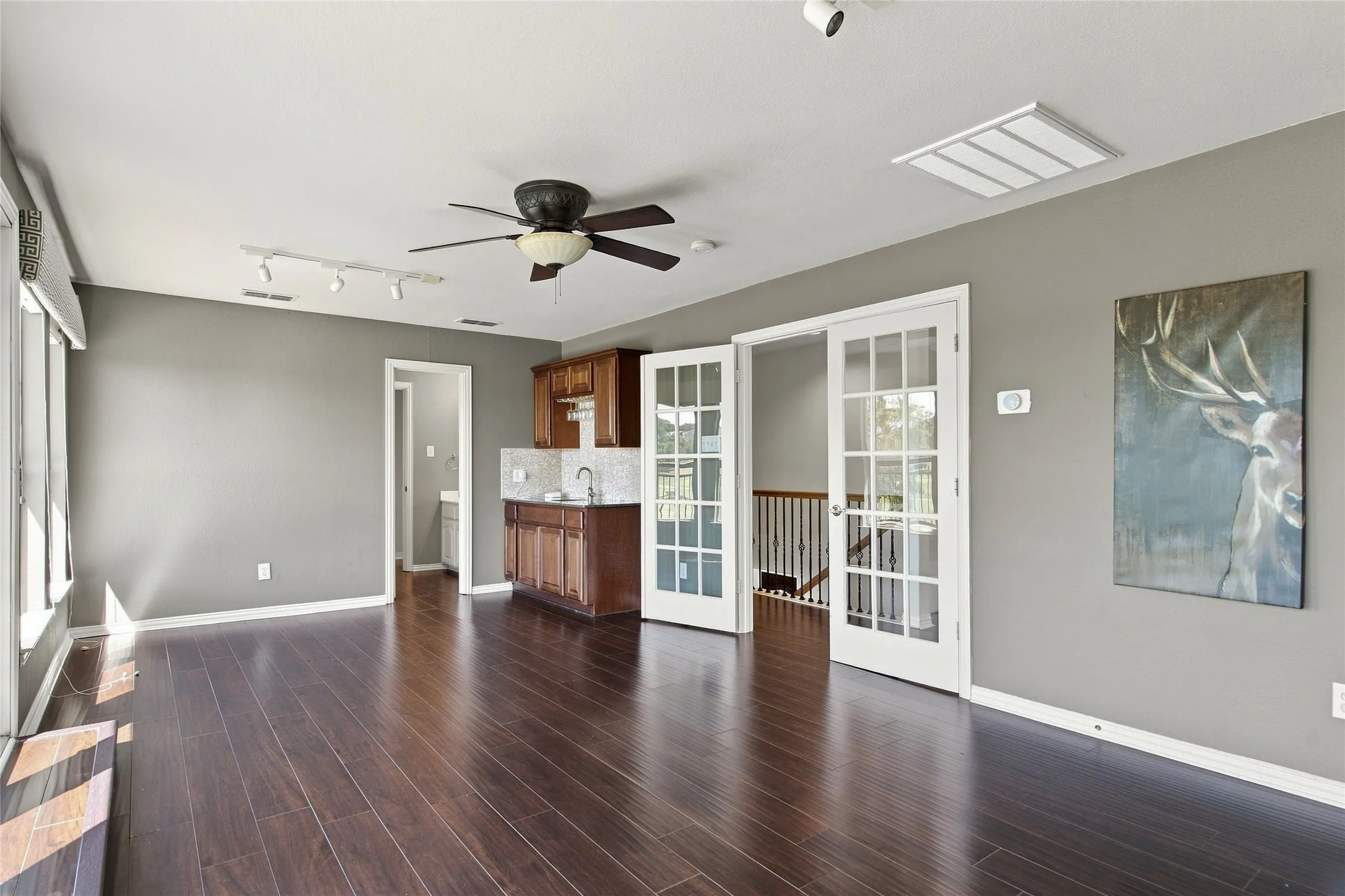 Features ceiling fan with integrated lighting, built-in wet bar with cabinetry and tile backsplash, and white French doors with glass panels.