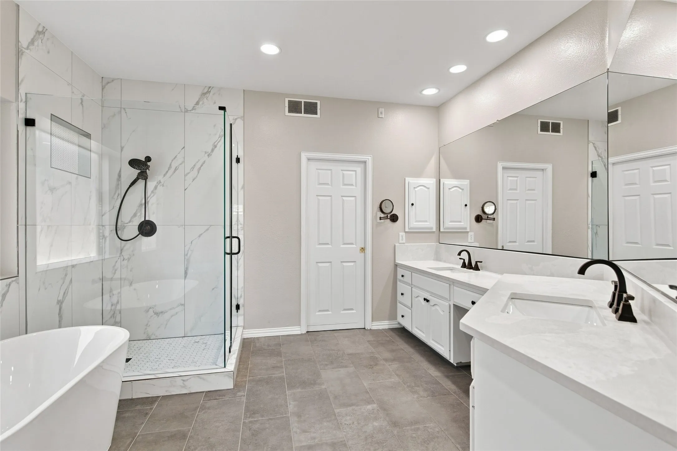 Walk-in shower with clear glass enclosure and tile surround, freestanding soaking tub, dual vanity with undermount sinks, and large wall-mounted mirror.