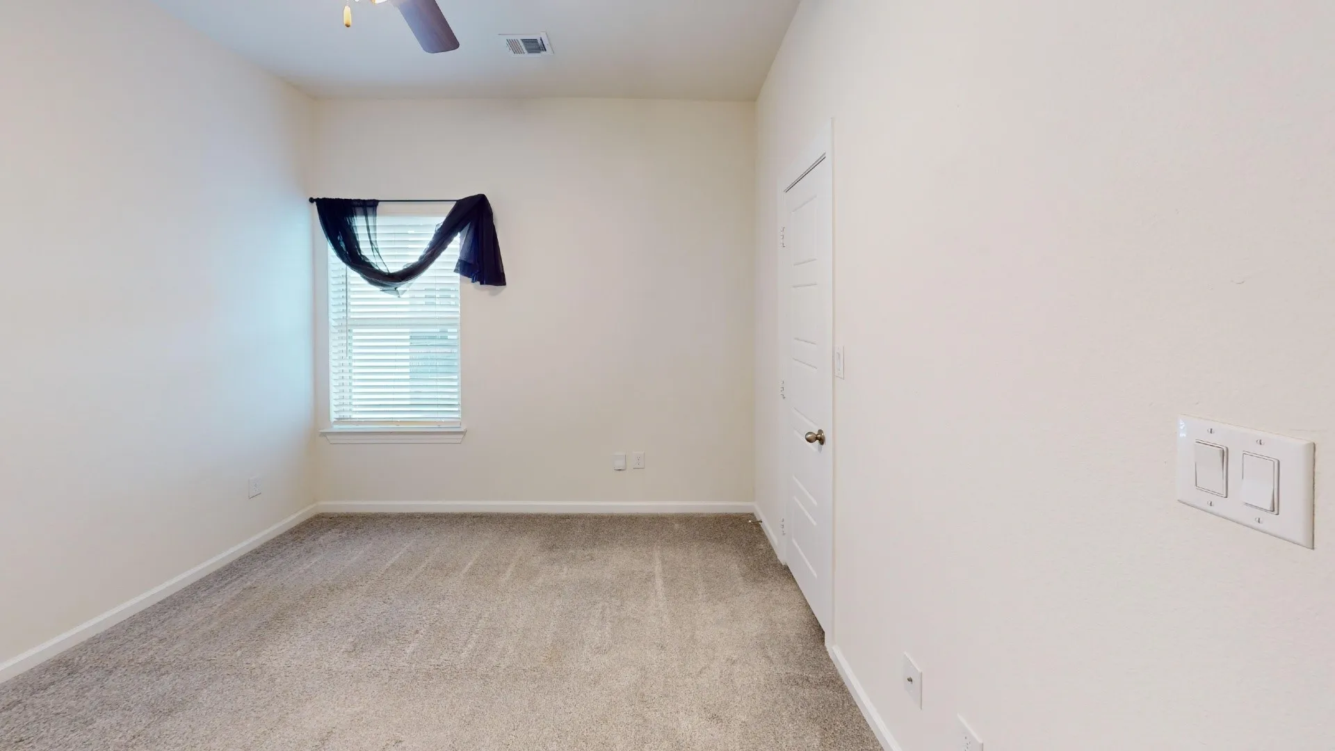 Plush carpeting, window with blinds, ceiling fan with integrated lighting, and a white paneled door