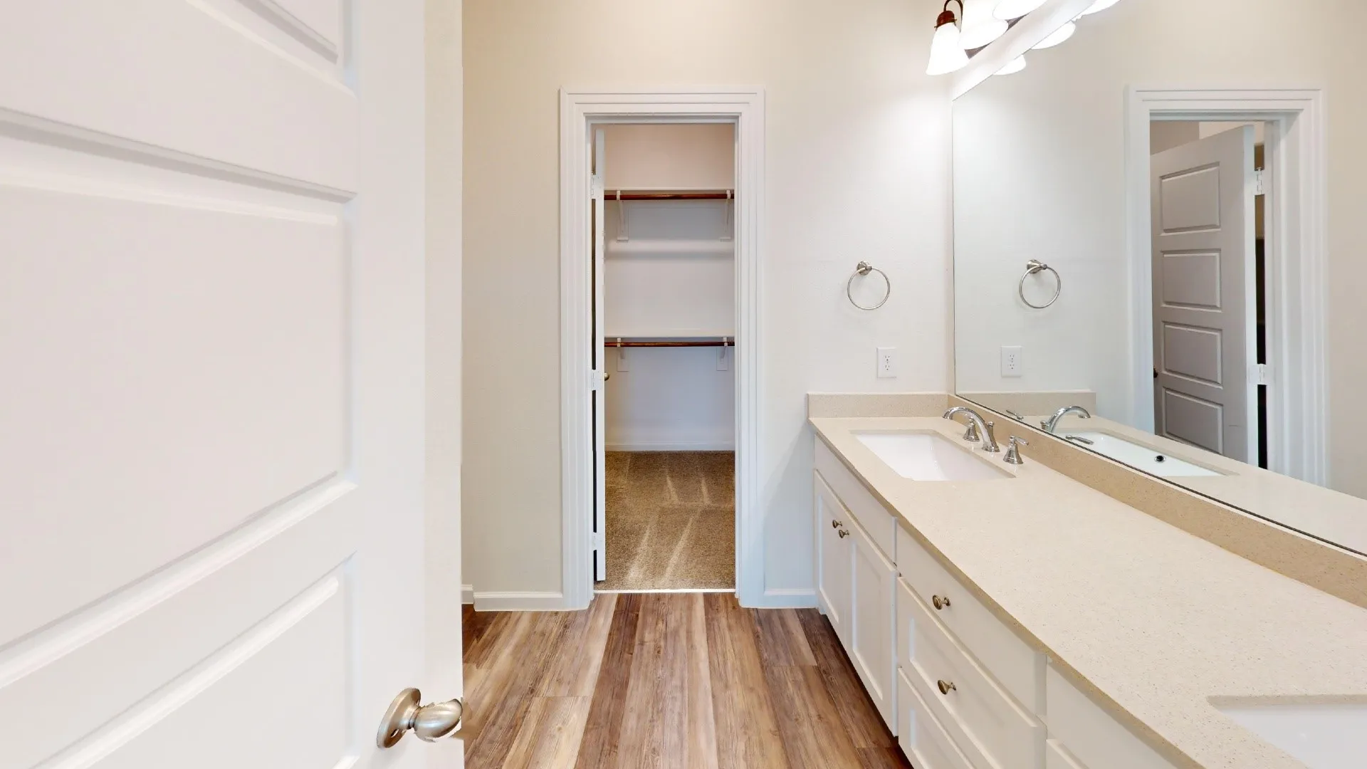 Double vanity with light-toned countertop, wood-finish flooring, and white cabinetry