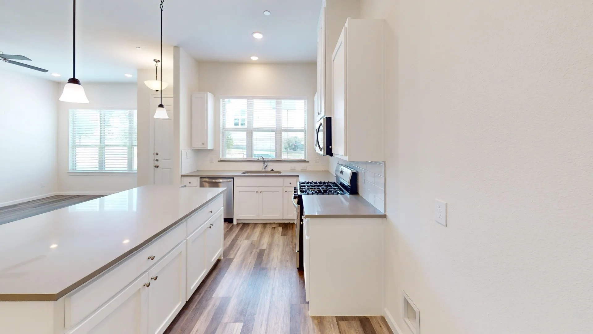 Modern galley kitchen featuring white cabinetry, stainless steel appliances, quartz countertops with waterfall edge, wood-finish flooring, and pendant lighting over the island workspace
