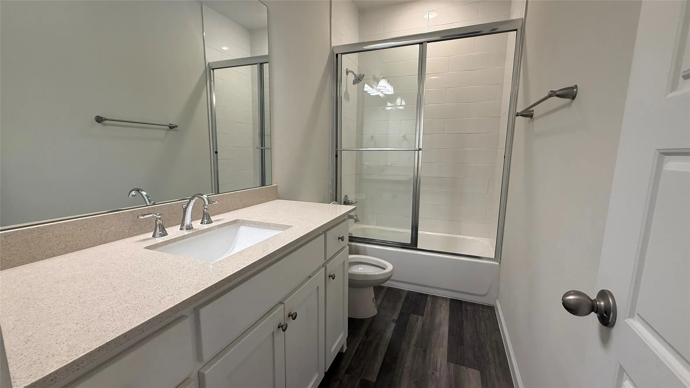 Bathroom featuring an integrated sink, polished chrome fixtures, a shower-tub combination with sliding glass doors, white subway tile surround, and wood-finish flooring
