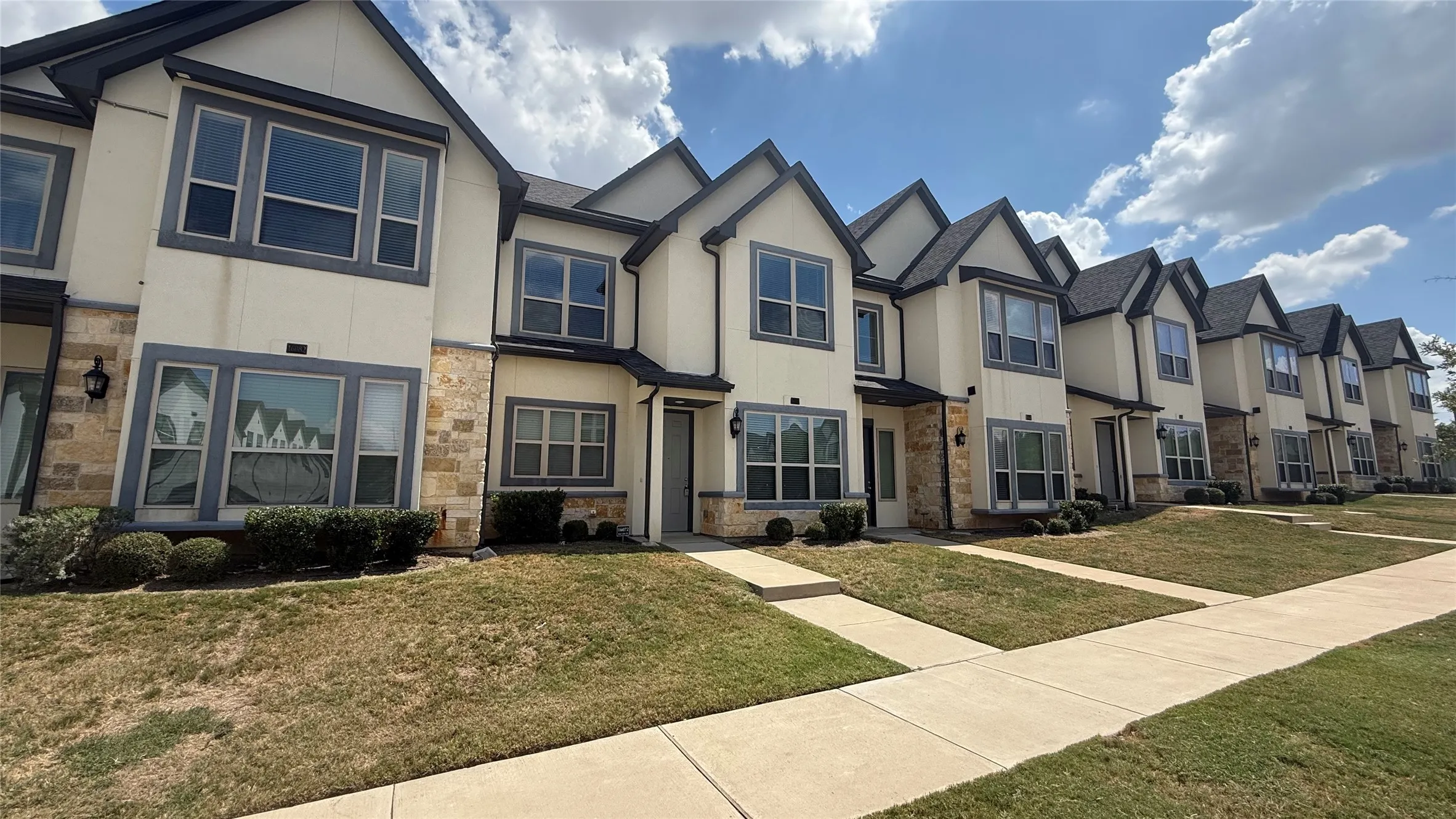 Contemporary townhomes featuring stone veneer accents, gabled roofs, and landscaped entryways