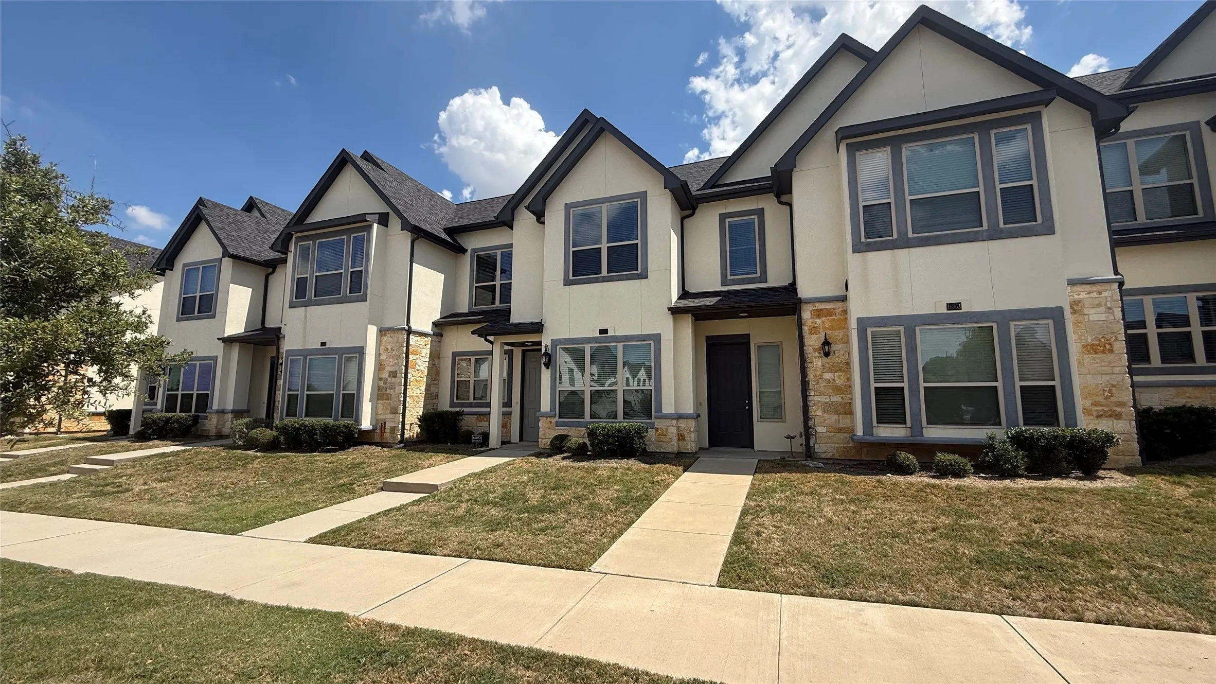 Stucco exterior with stone accents, dark trim windows, gabled rooflines, and a concrete walkway