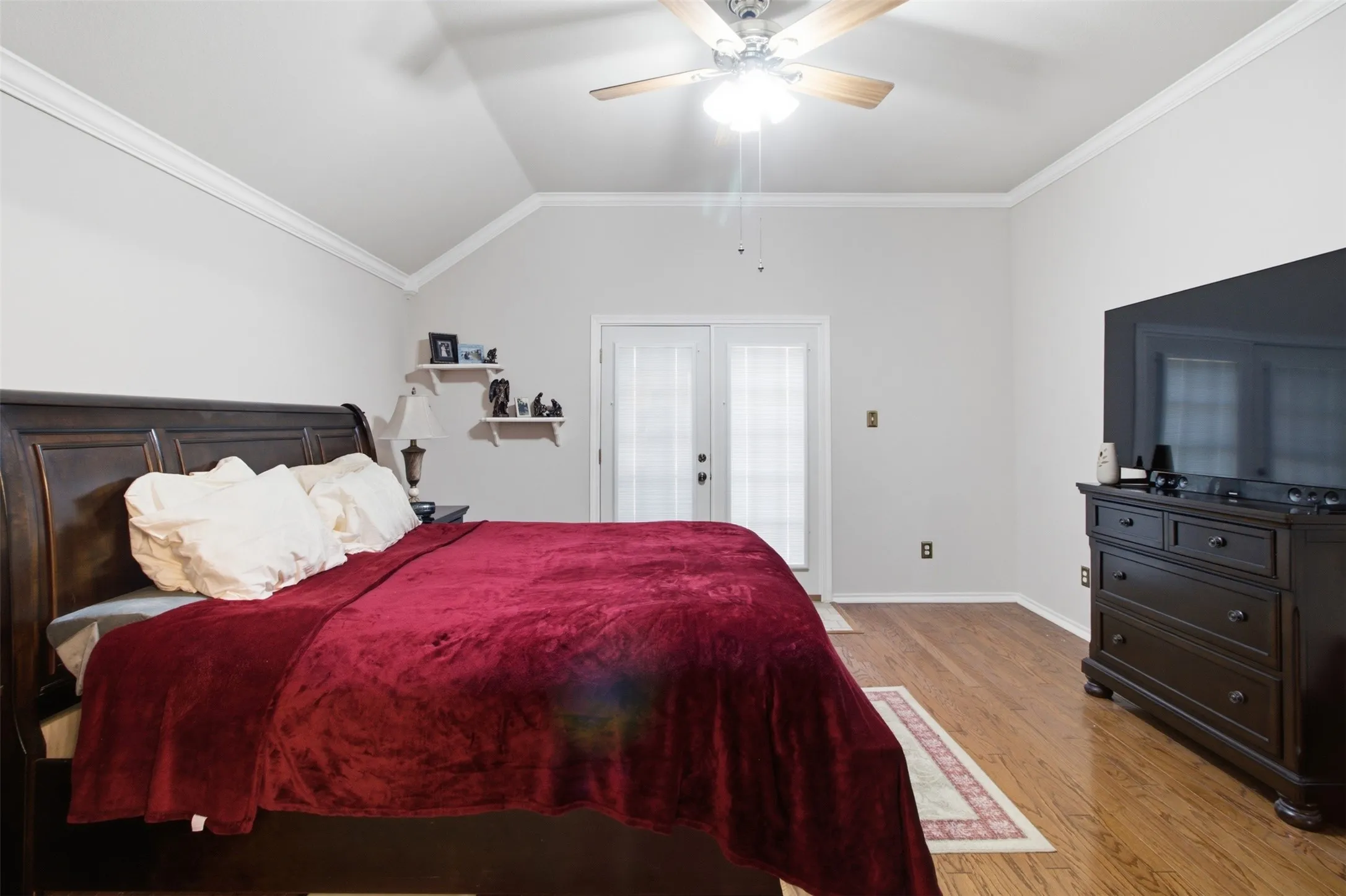 Vaulted ceiling with crown molding, wood-finish flooring, and a ceiling fan