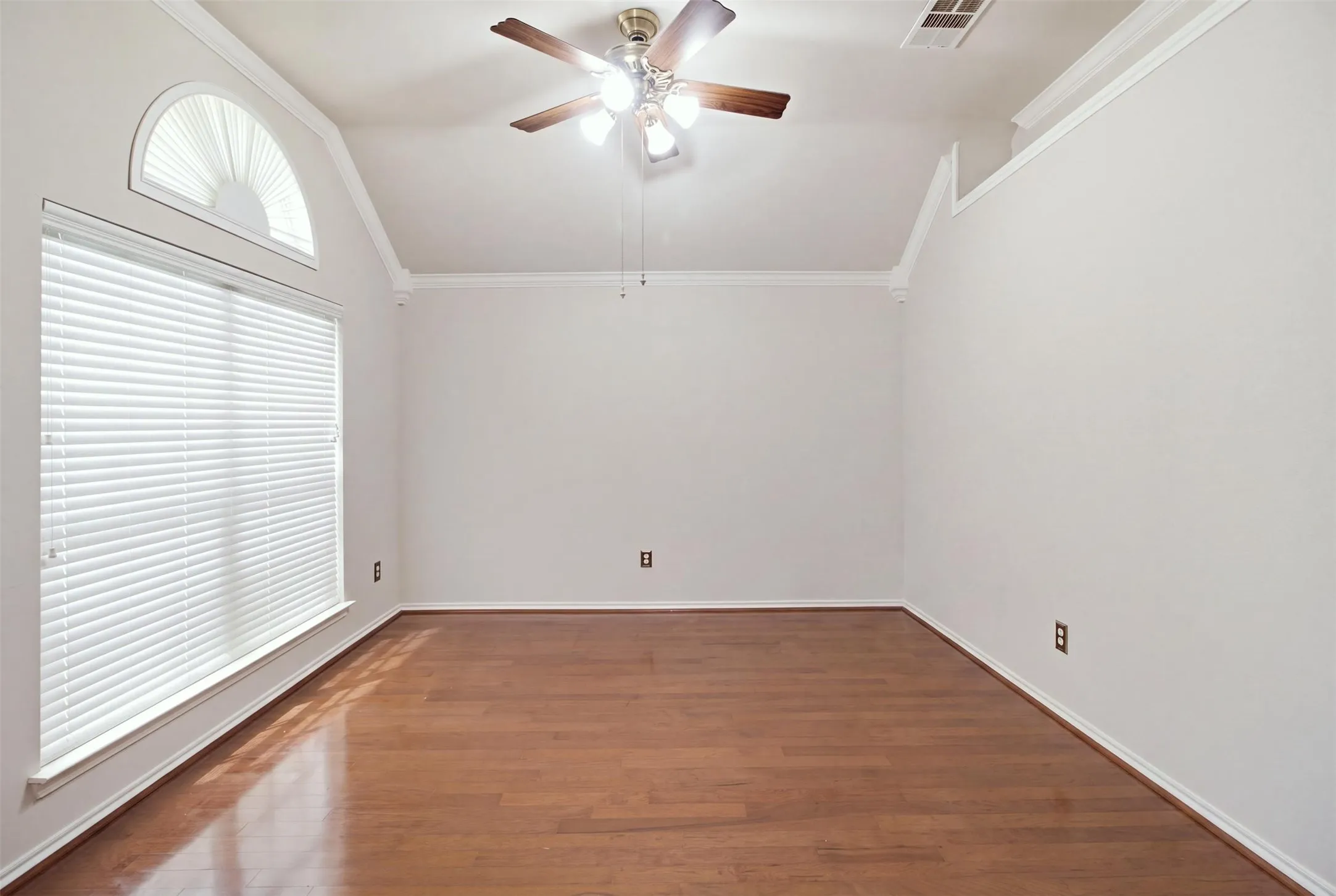 Vaulted ceiling with crown molding, wood-finish flooring, large window with blinds, and an arched transom window