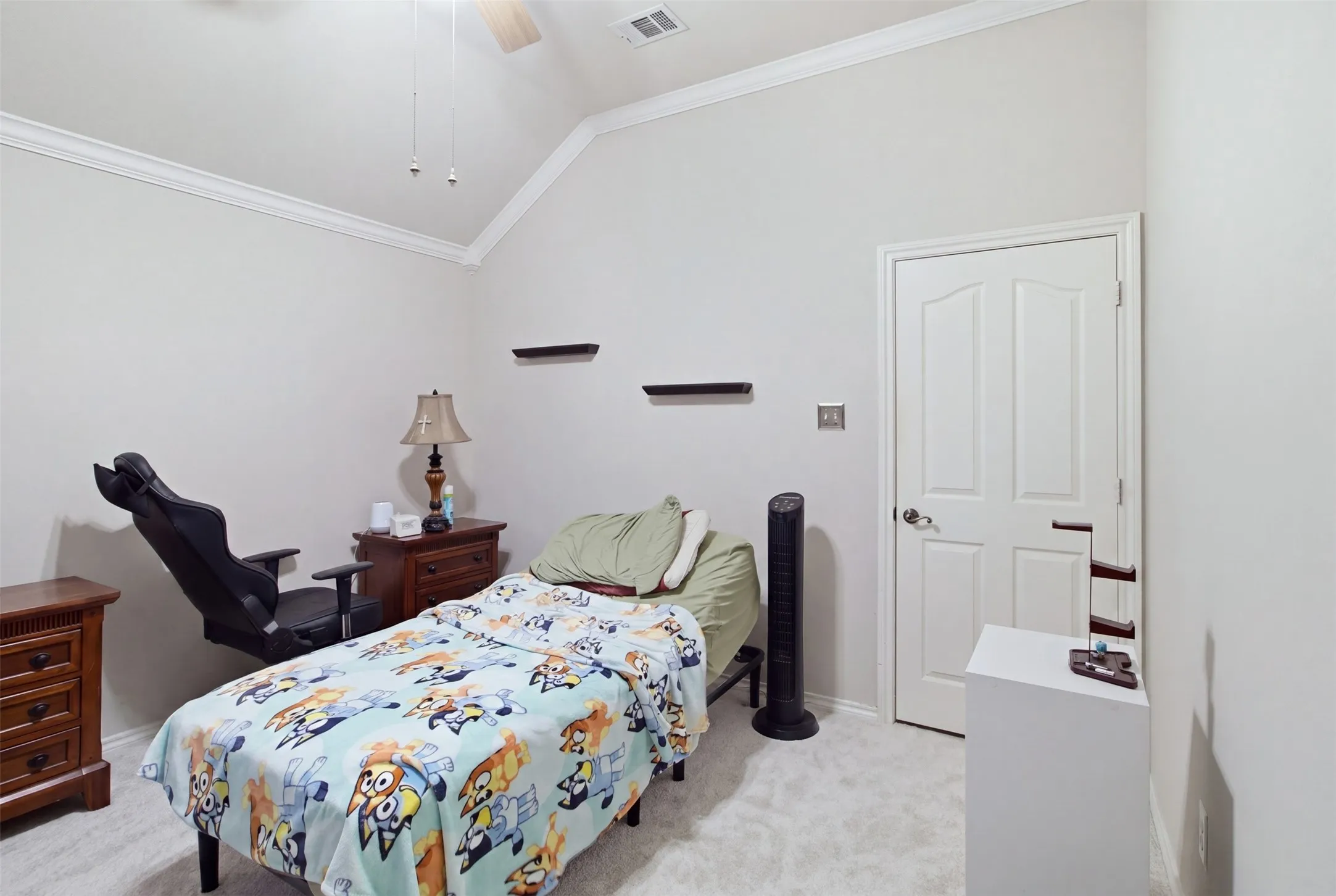 Vaulted ceiling with crown molding, ceiling fan, carpet flooring, and a paneled door