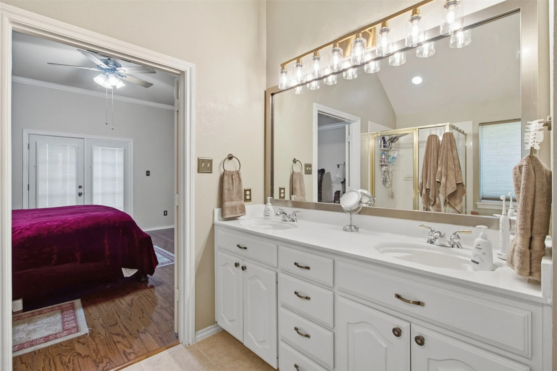 Dual vanity with white cabinetry, polished chrome fixtures, and an expansive wall mirror with a multi-bulb light bar