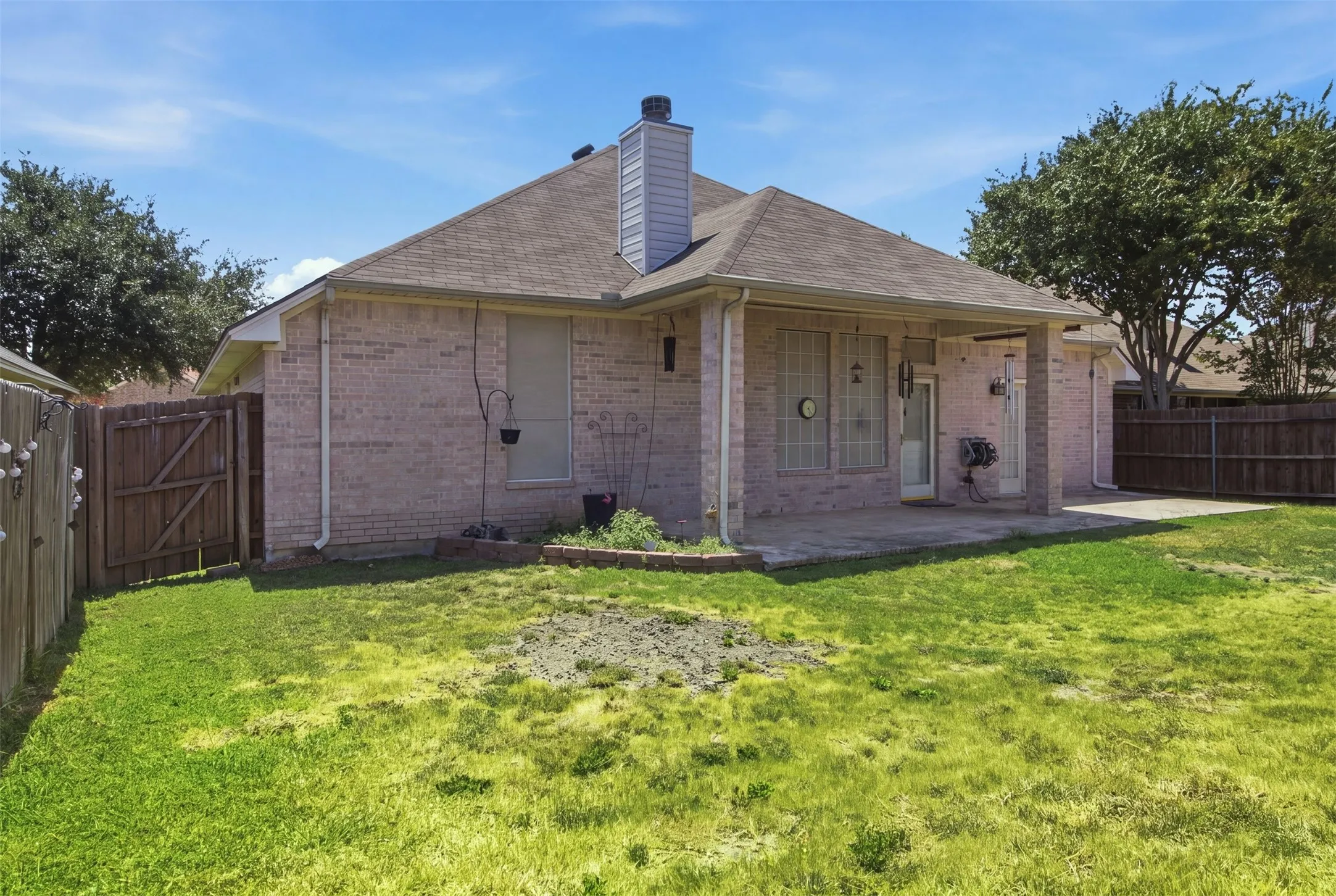 Rear exterior featuring brick facade, covered patio, concrete patio extension, and fenced perimeter