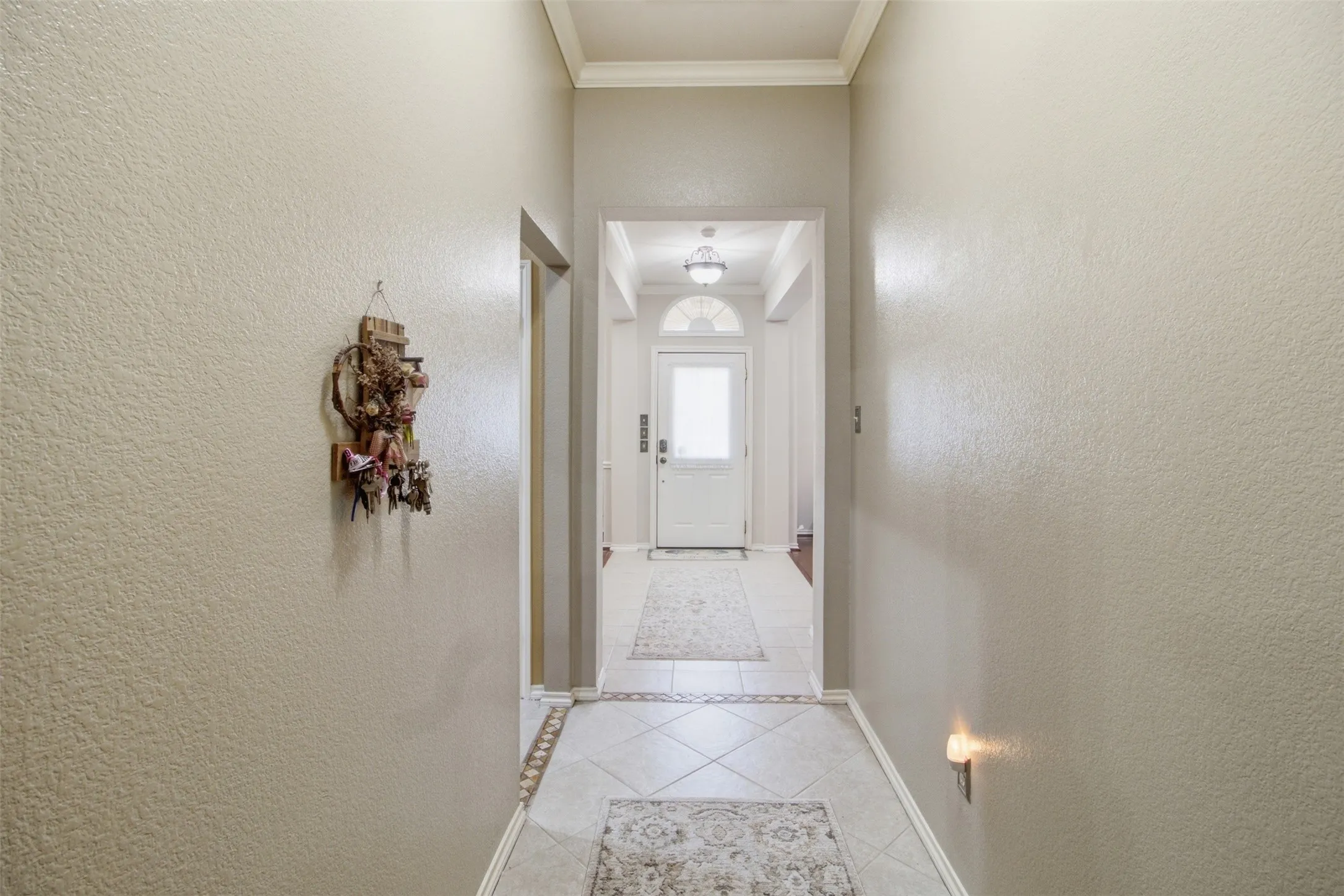 Hallway featuring light-toned textured walls, crown molding, and decorative tile flooring