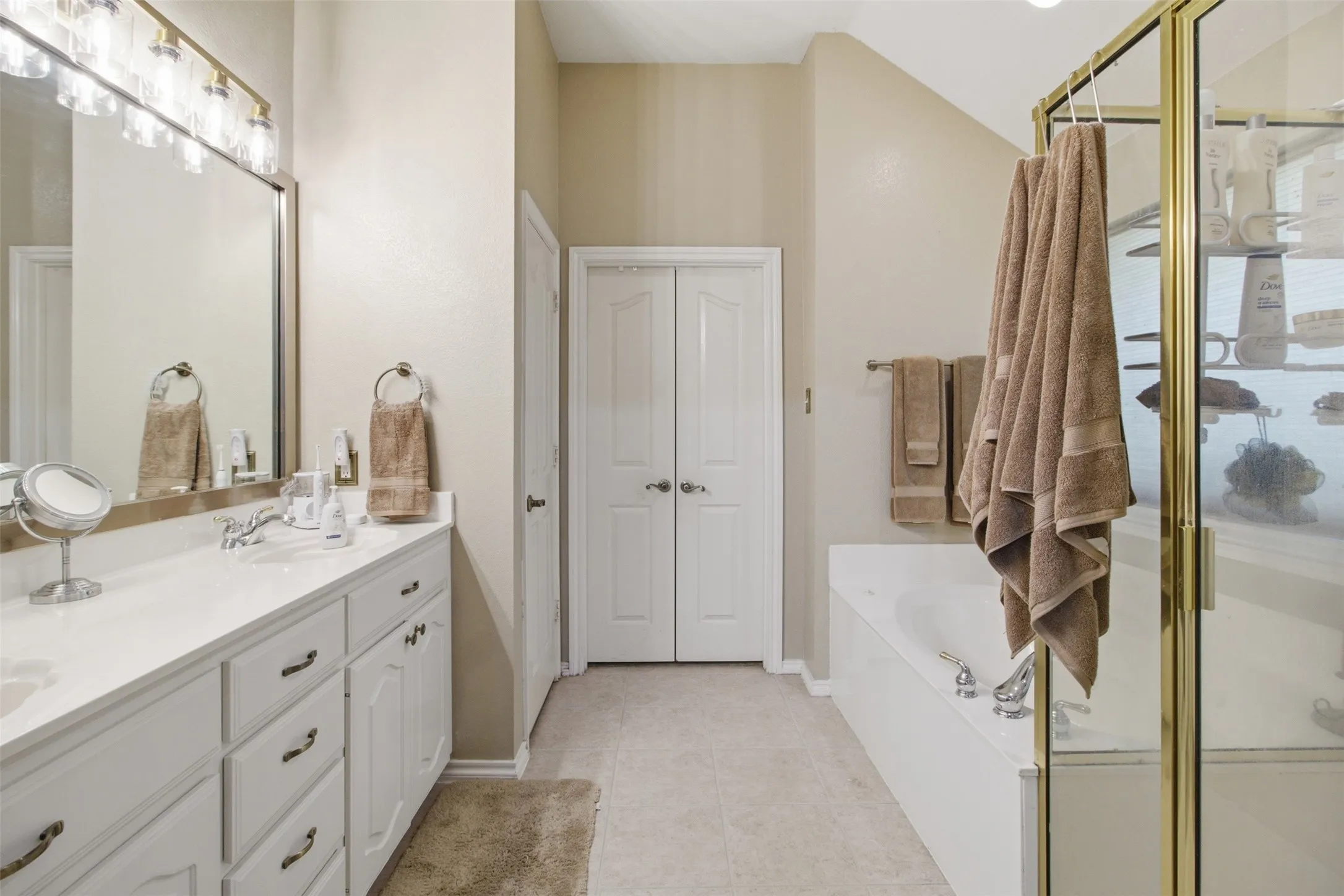 Dual vanity with white cabinetry and chrome hardware, an integrated soaking tub, a separate glass-enclosed shower, and tile flooring