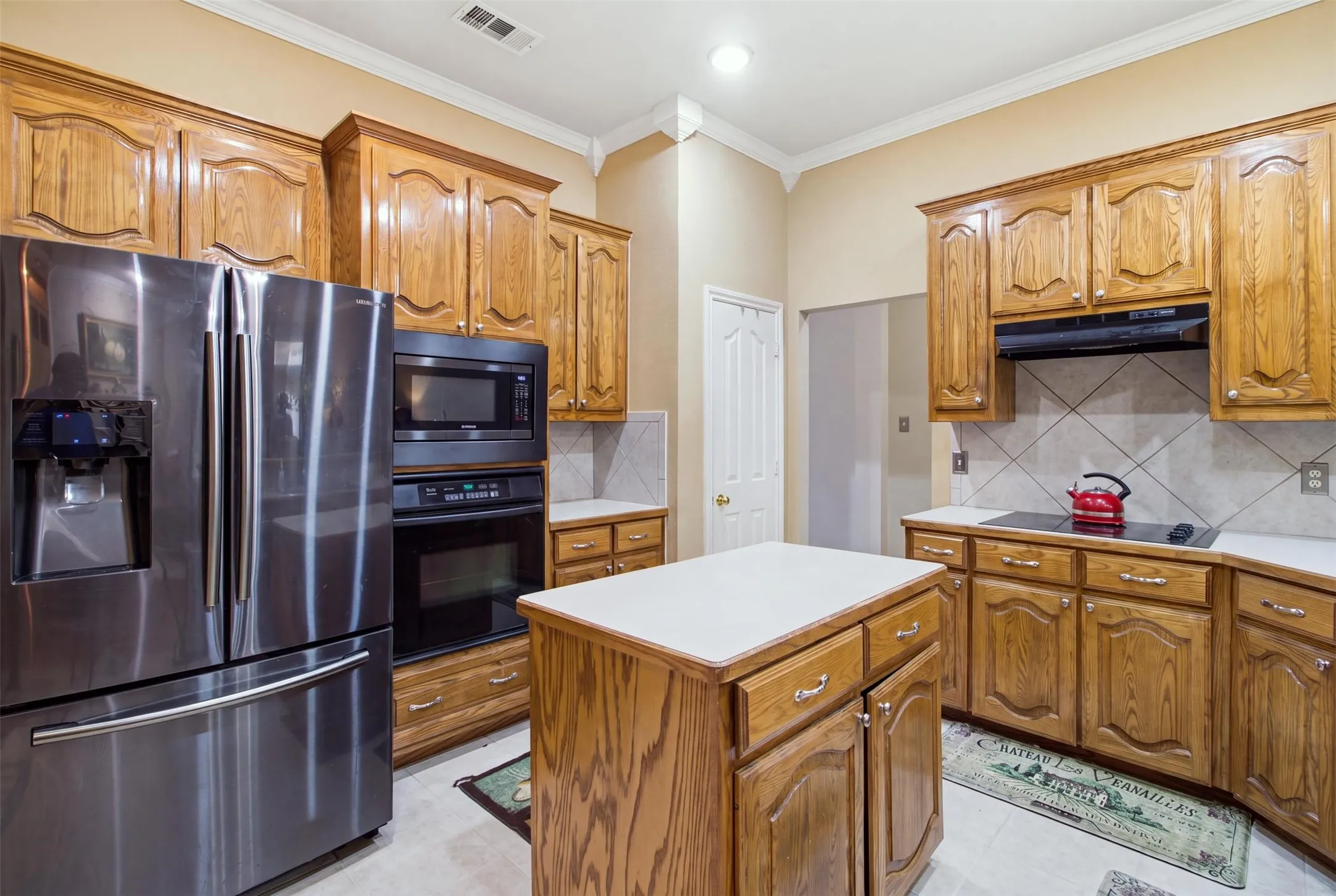 Kitchen featuring wood cabinetry, stainless steel appliances, a center island with countertop, tile flooring, and a tile backsplash