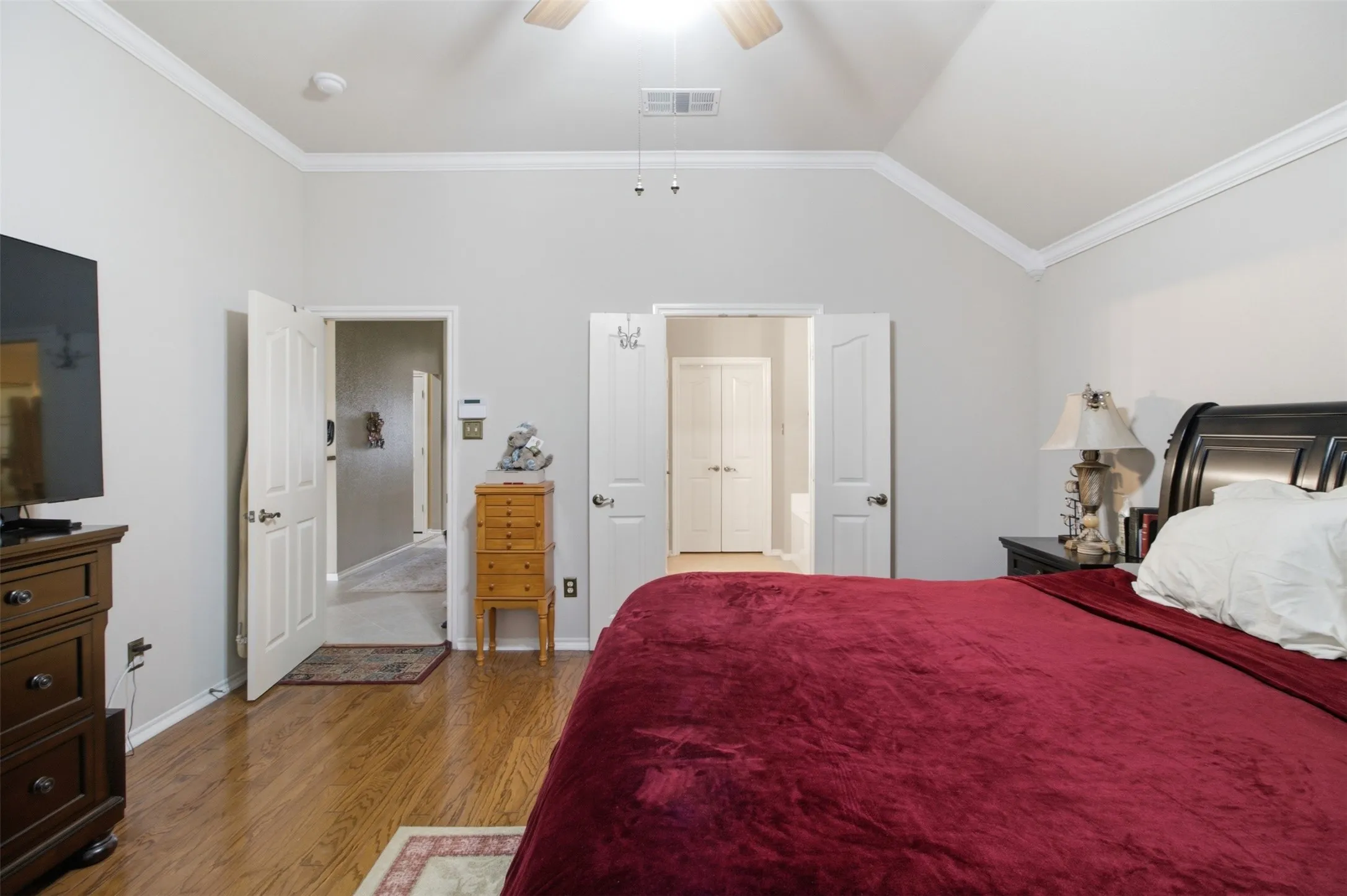 Vaulted ceiling with a ceiling fan, crown molding, wood-finish flooring, and white paneled doors