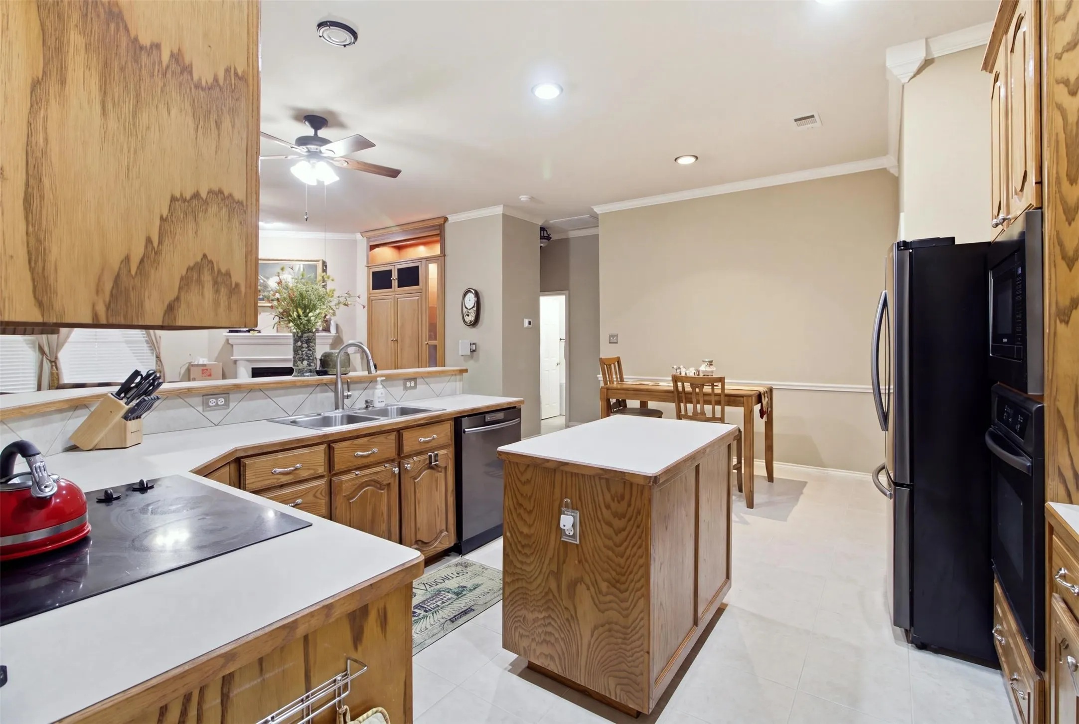 Kitchen with wood-finish cabinetry, light-toned countertops, tile backsplash, and stainless steel dishwasher