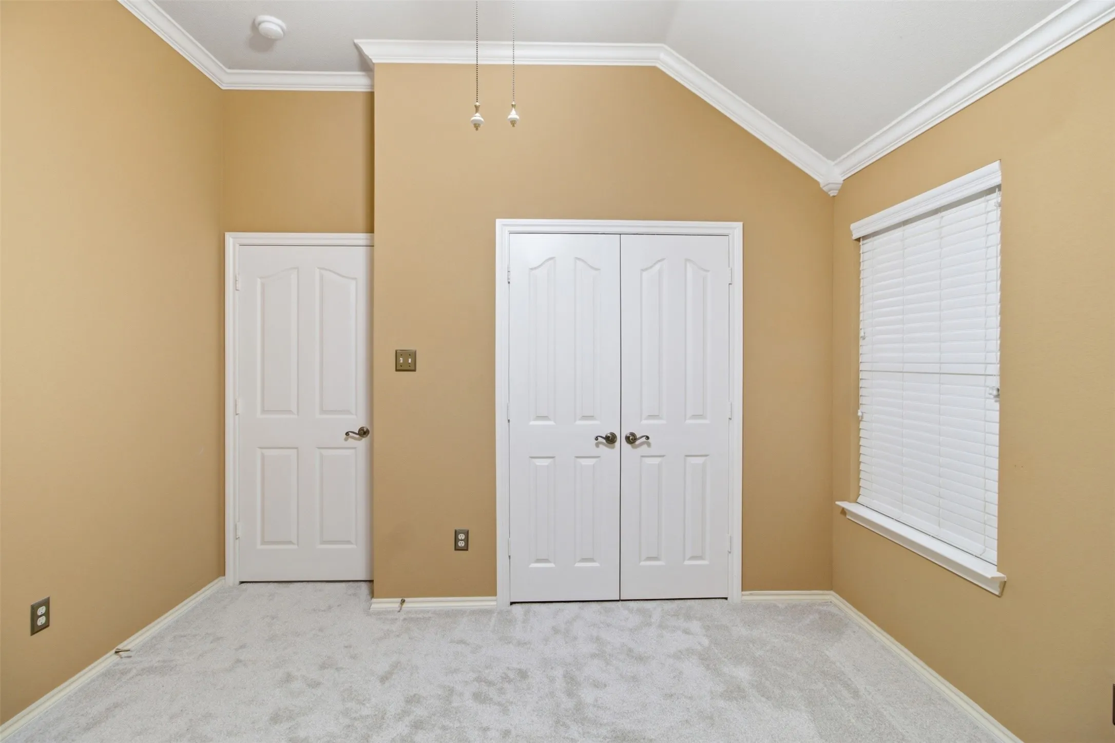 Vaulted ceiling with crown molding, double bifold closet doors, and light-colored carpeting