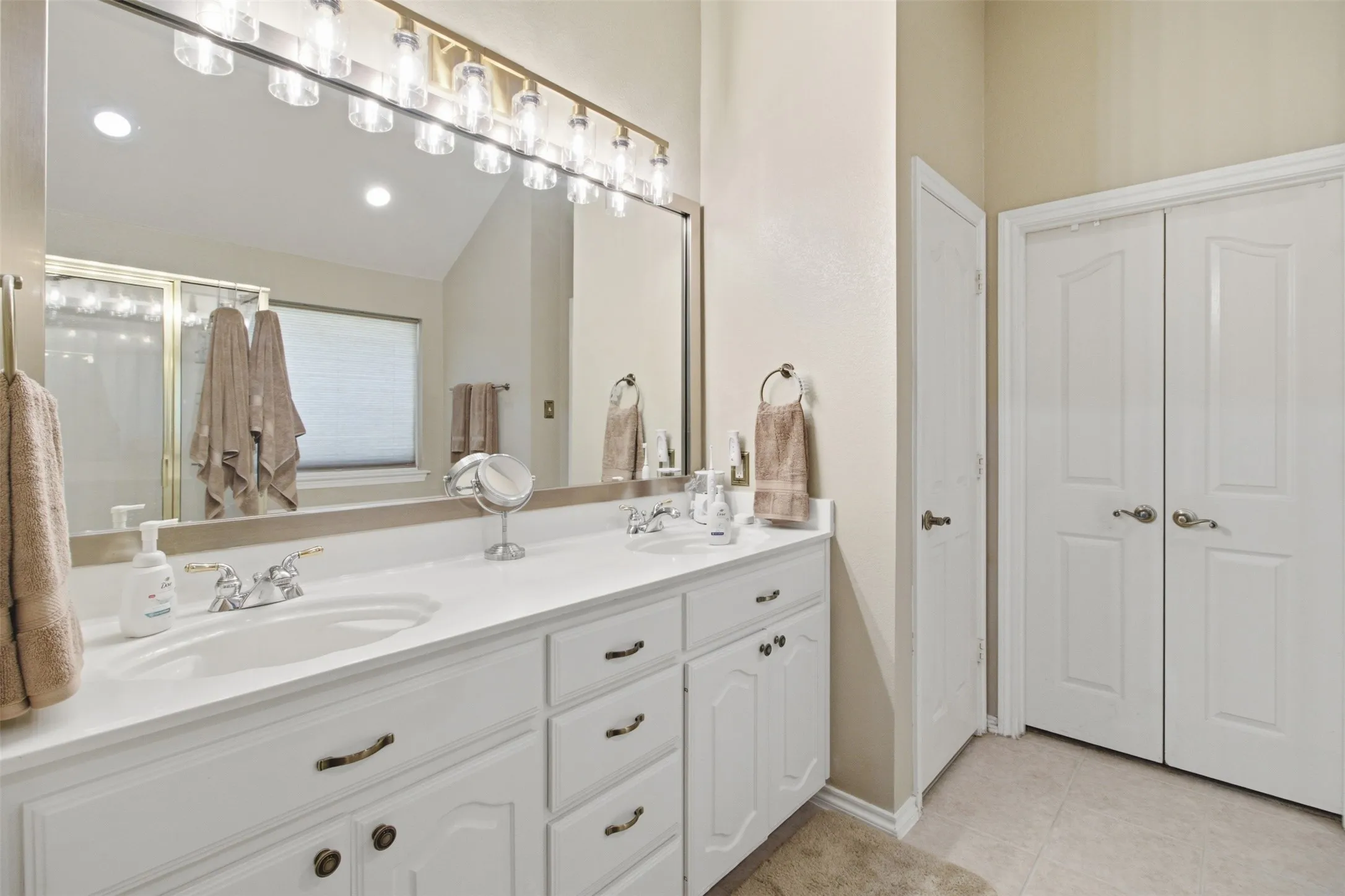 Dual vanity with white cabinetry, integrated sinks, chrome faucets, and an expansive mirror