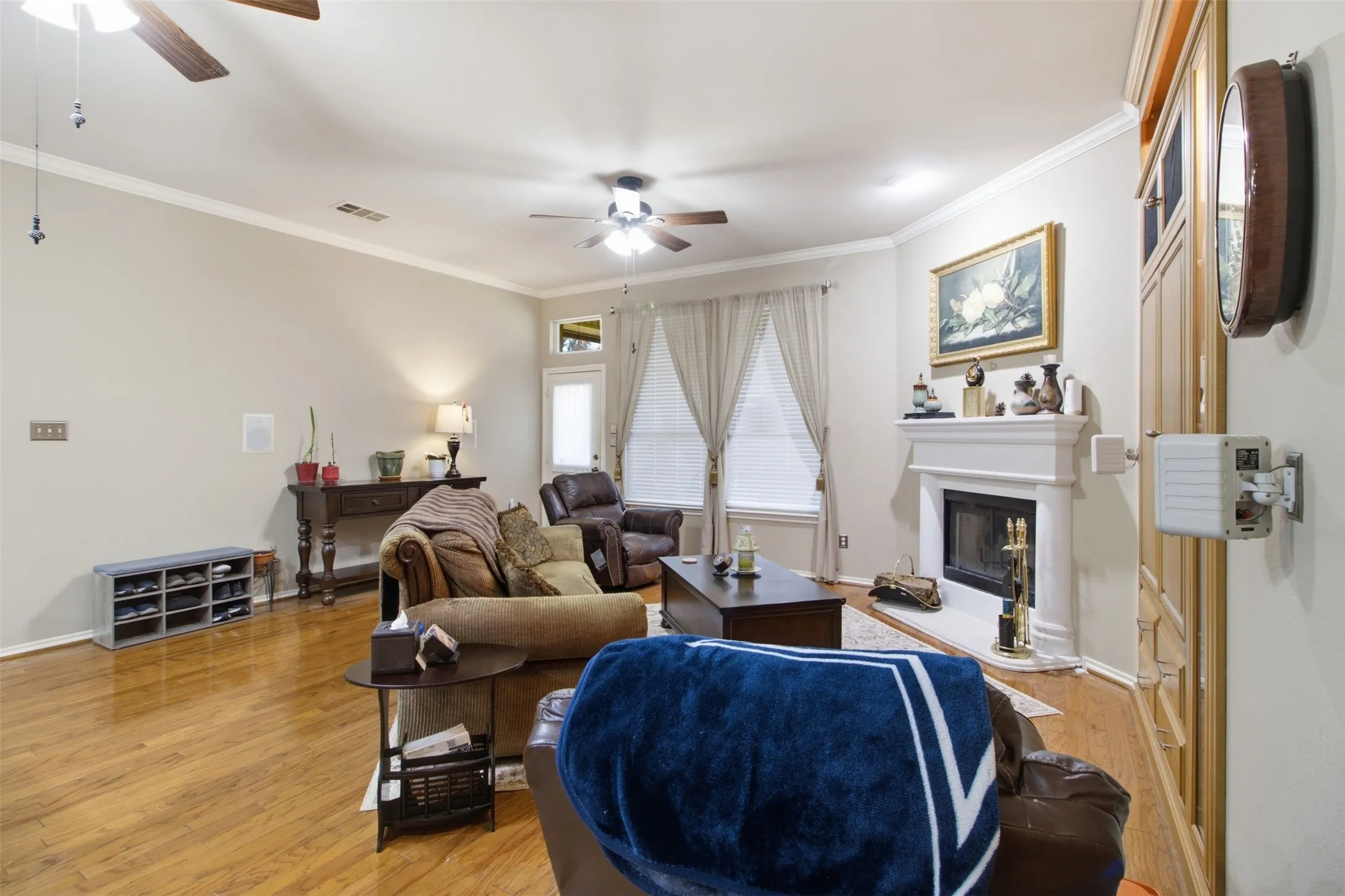 Living space featuring wood flooring, a fireplace with a mantel, crown molding, and ceiling fans