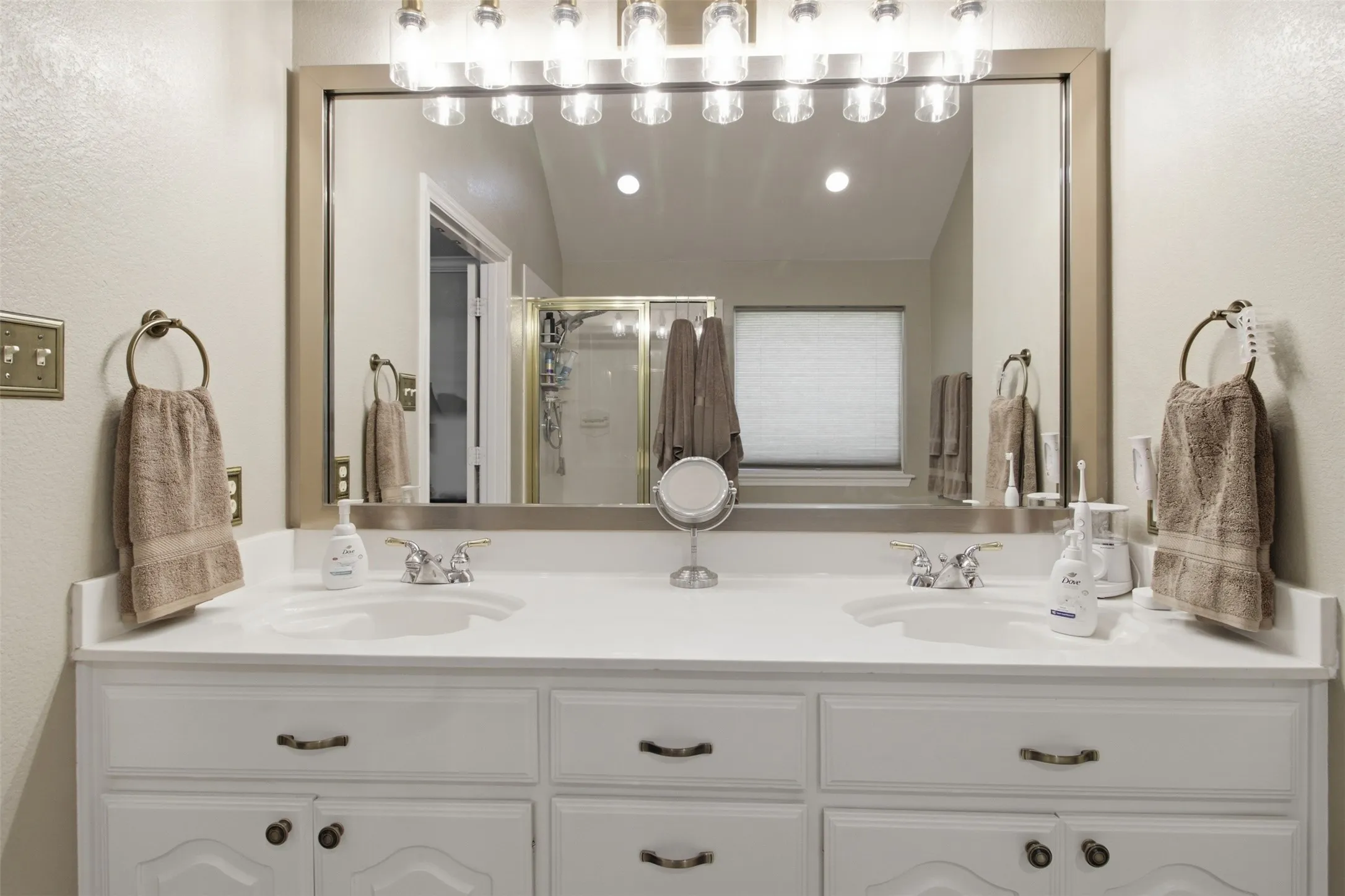 Dual vanity with white cabinetry, integrated sinks, brushed nickel faucets, and a large framed mirror with overhead lighting
