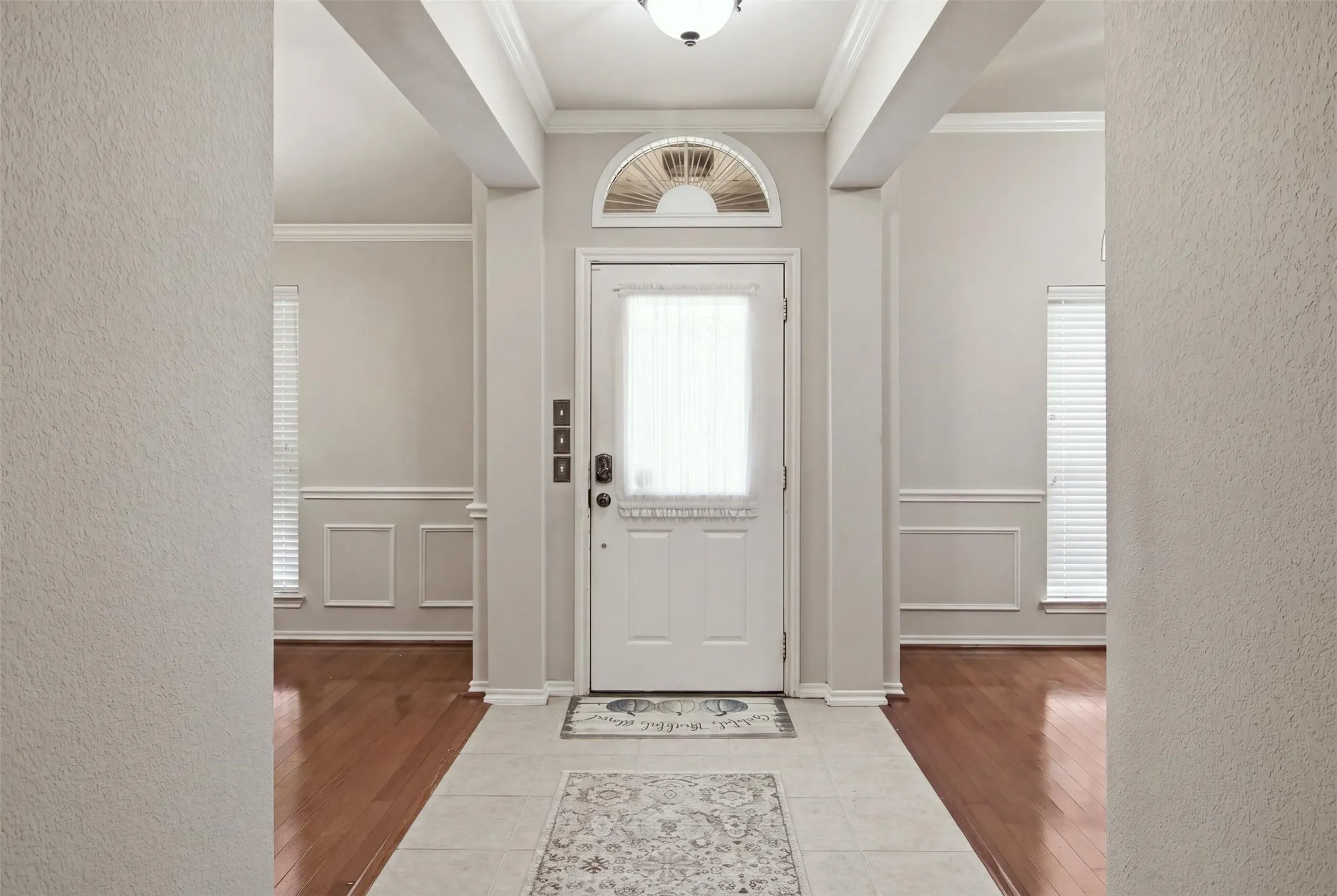 Entryway featuring a decorative transom window, overhead flush mount light, tile flooring, and wood-finish flooring