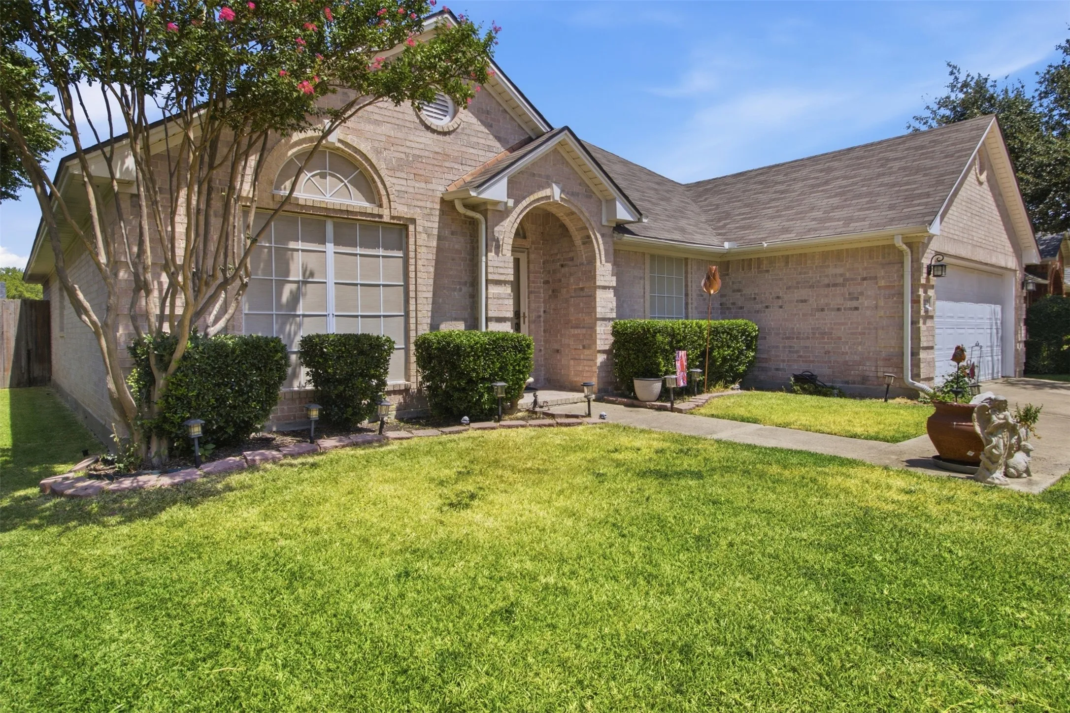 Brick exterior with an arched entry, prominent front-facing window with an arched transom, and a two-car garage