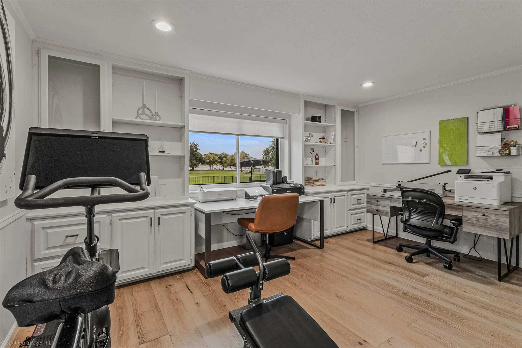 Wood-finish flooring, built-in white cabinetry, recessed lighting, and a large window overlooking green space