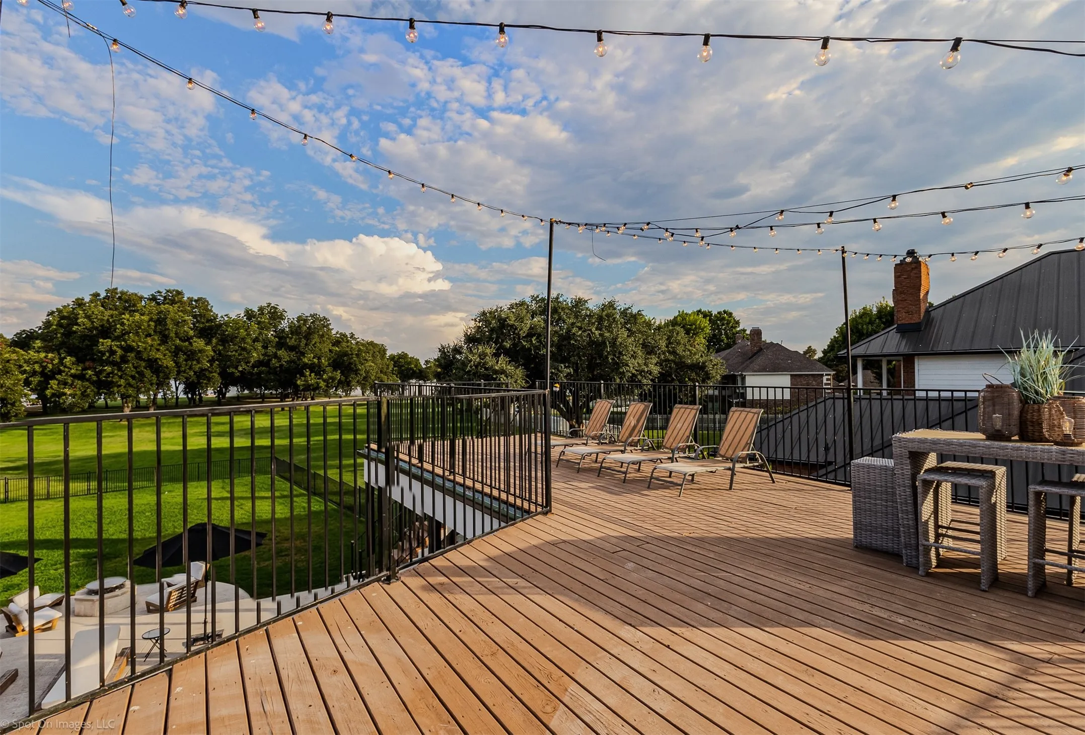 Expansive outdoor deck featuring wood-finish flooring, black metal railings, and string lighting