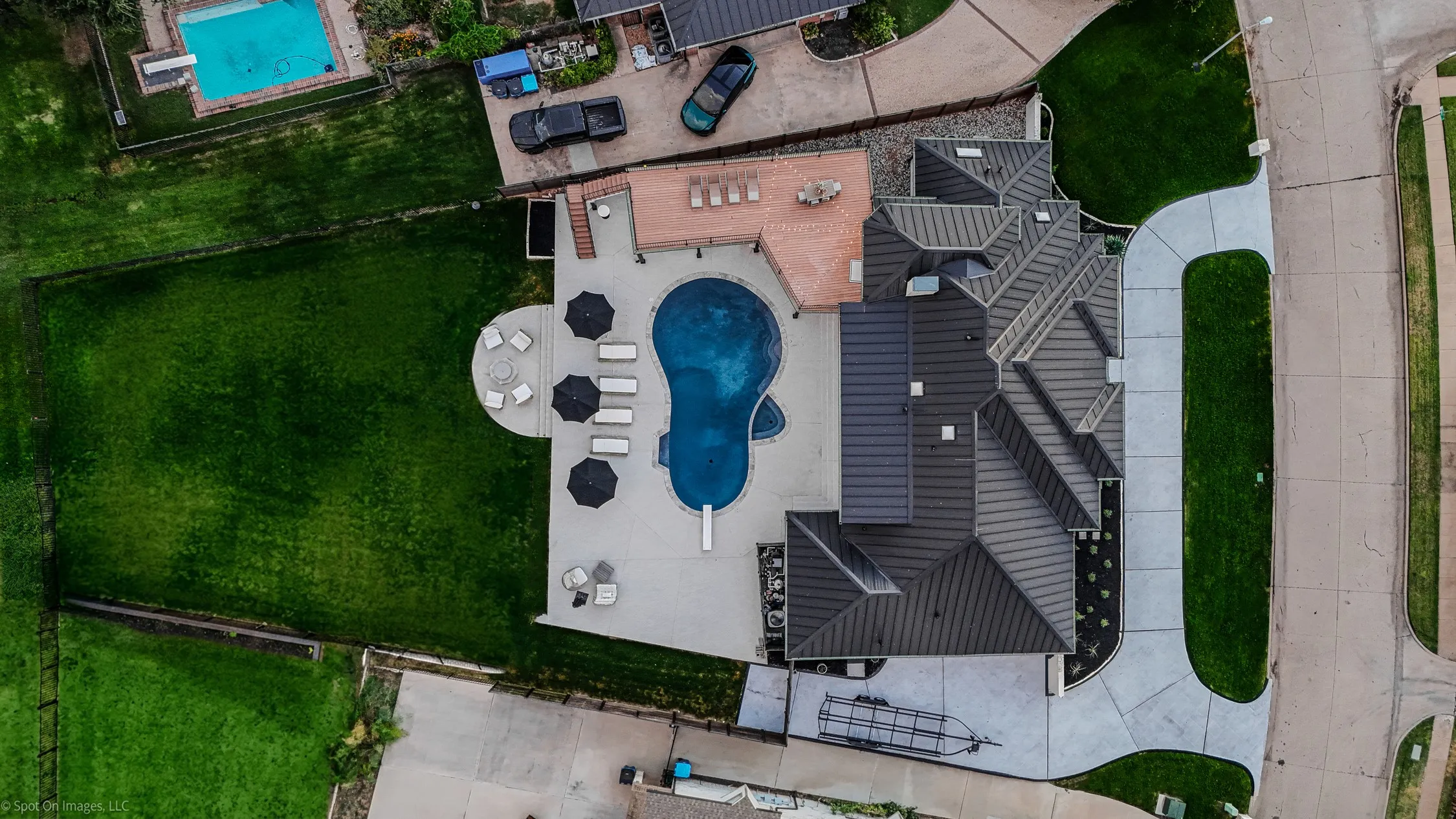 Custom swimming pool with integrated diving board, expansive concrete patio, outdoor decking, and a large manicured lawn