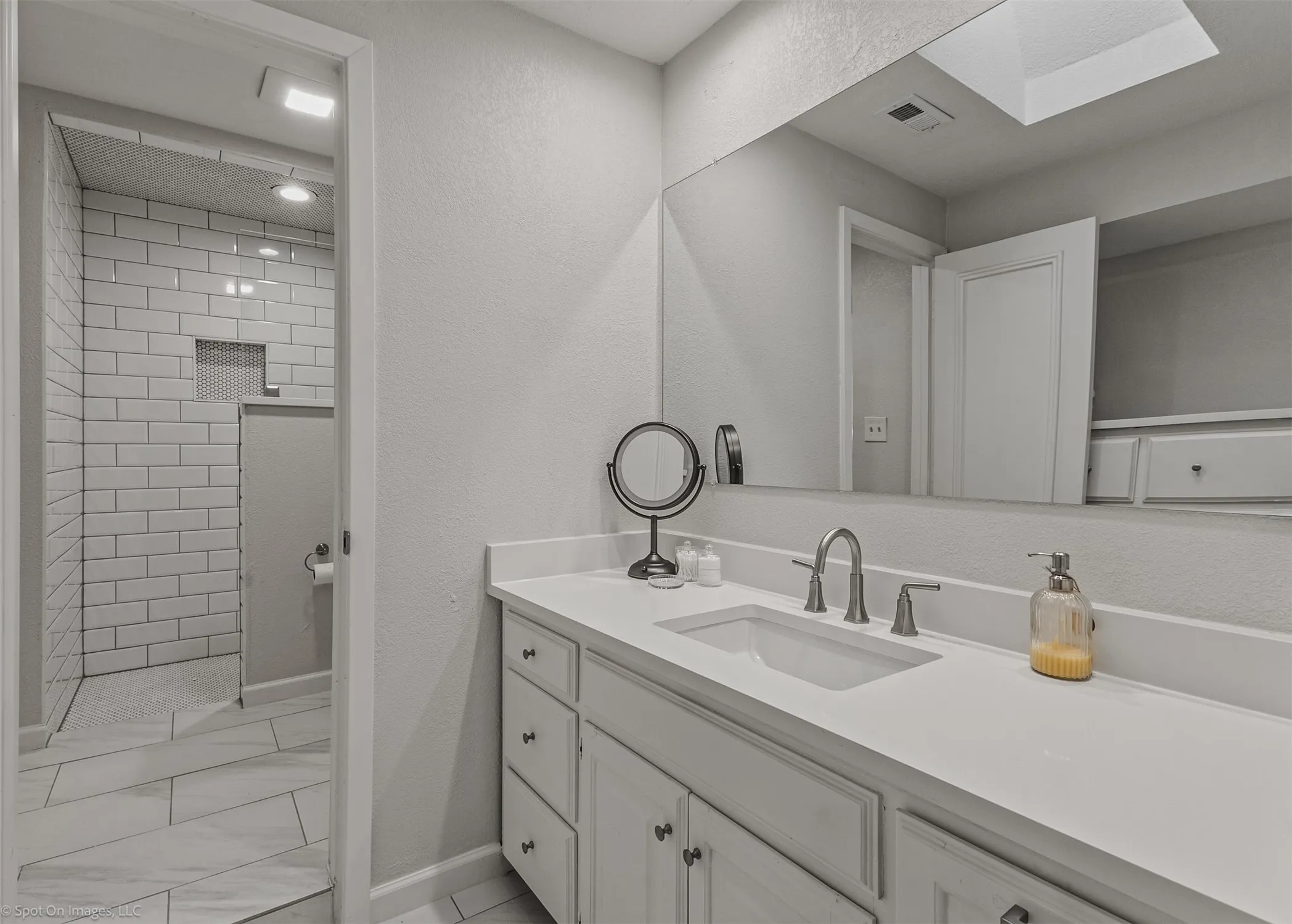 Bathroom featuring a single vanity with an integrated sink, a large wall-mounted mirror, and a walk-in shower with subway tile