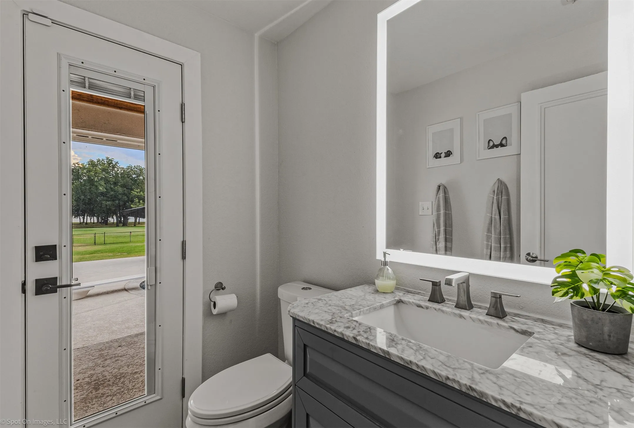 Bathroom featuring a white toilet, full-lite door, vanity with a stone countertop, undermount sink, and an illuminated mirror