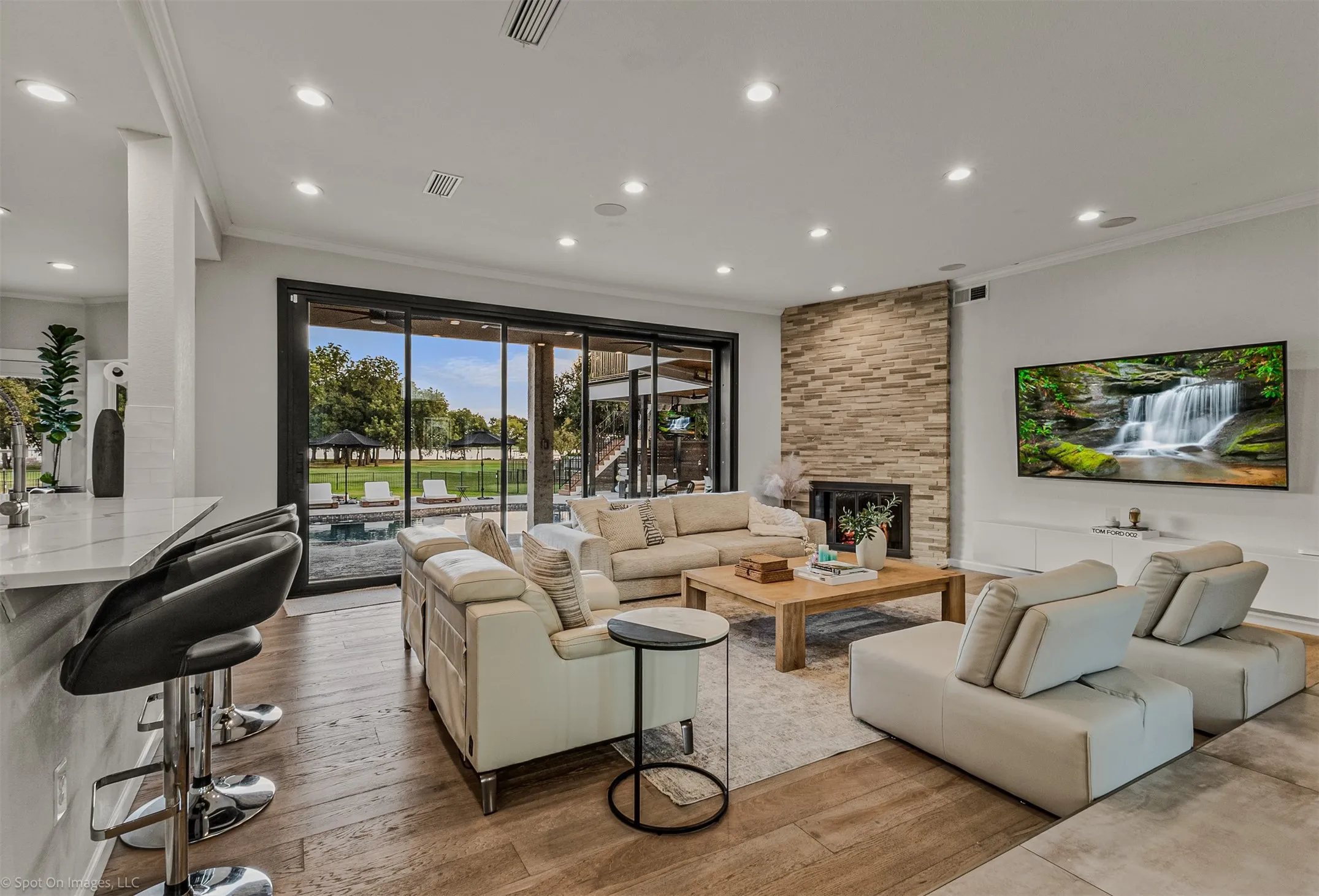 Spacious living area featuring wood-finish flooring, a stone-clad fireplace, and recessed lighting