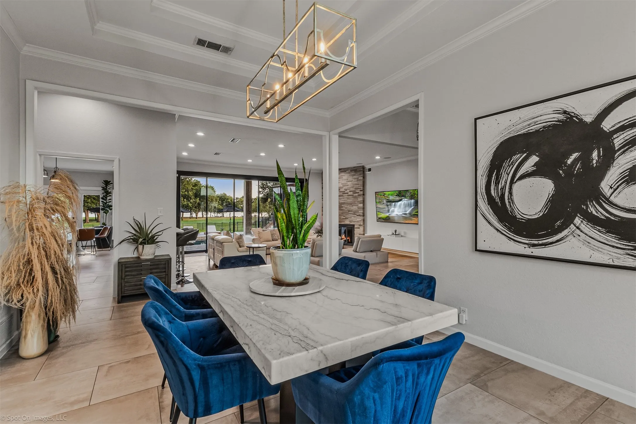Tray ceiling with crown molding, linear chandelier, light-toned tile flooring, and a marble-finish tabletop