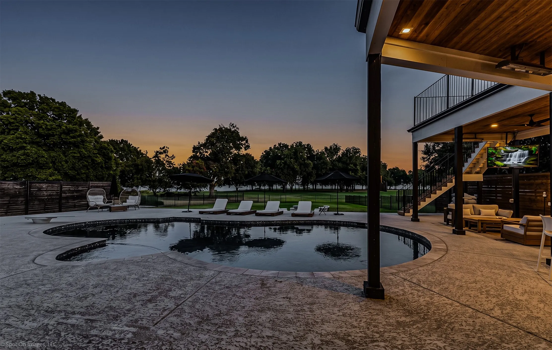 Freeform swimming pool with a stone coping, expansive stamped concrete patio, and an upper-level balcony with metal railings