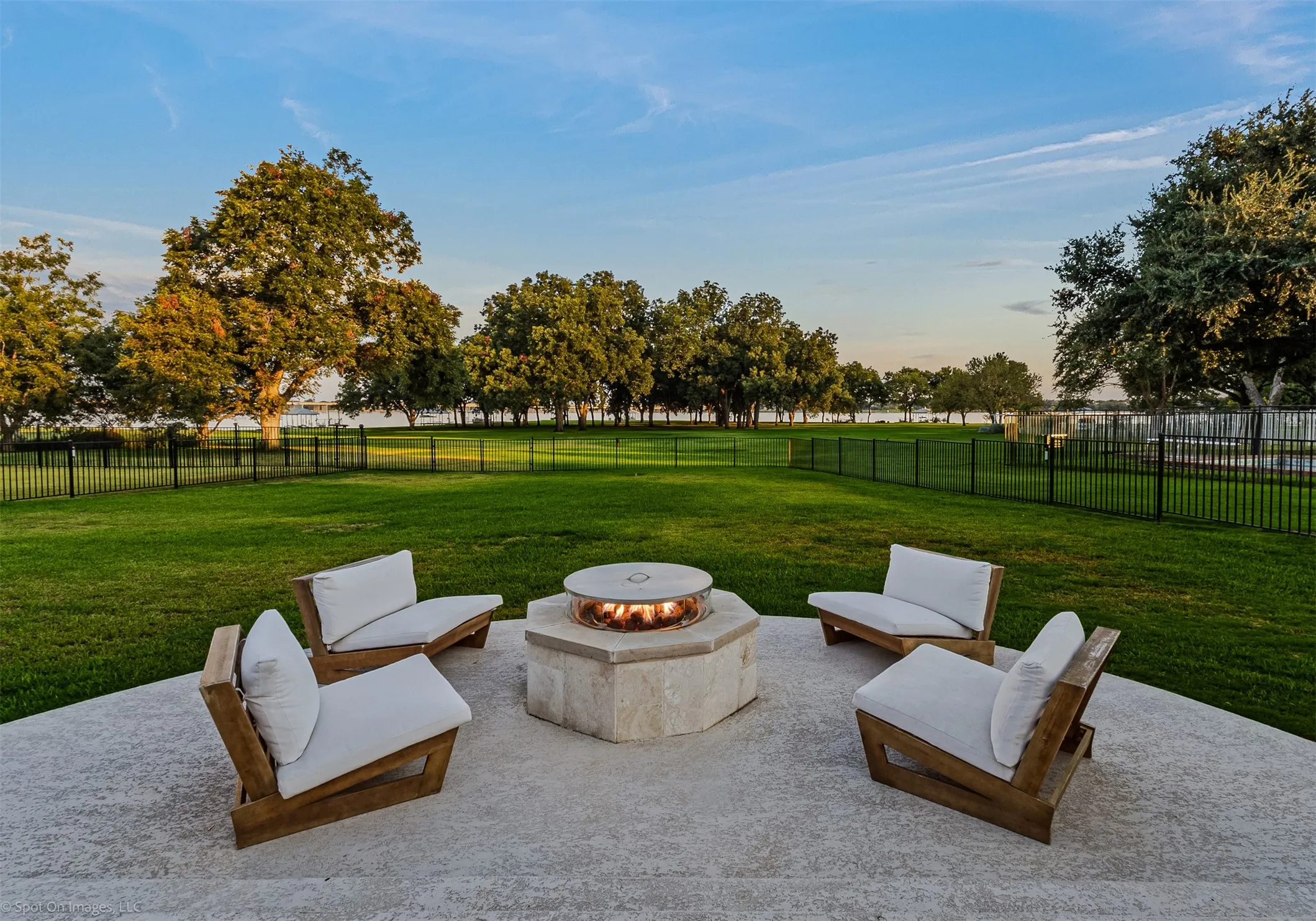 Expansive backyard featuring a stone fire pit, concrete patio, and a black metal fence