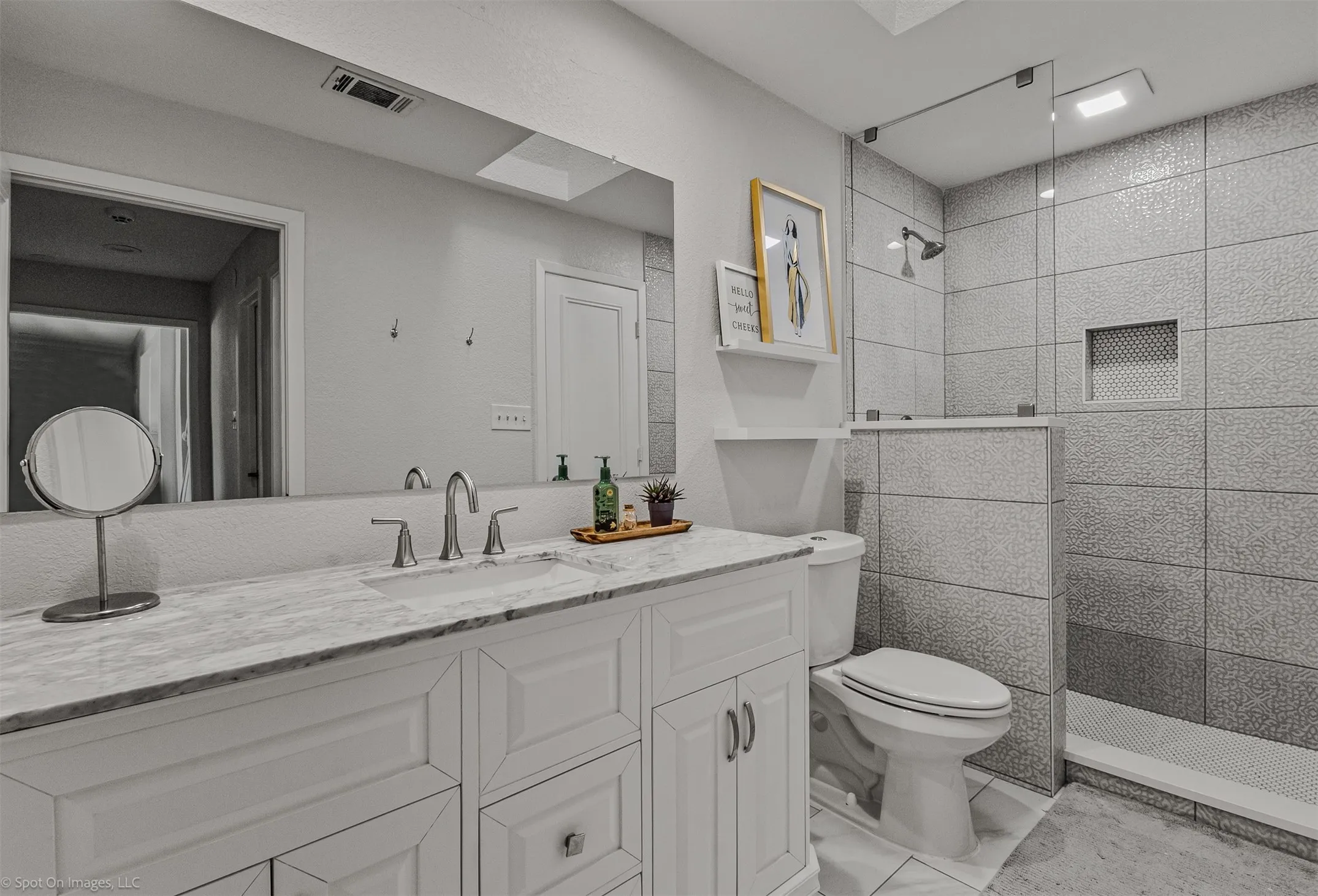 Vanity with integrated sink and chrome faucet, large rectangular mirror, walk-in shower with tiled walls, glass shower enclosure, and recessed shower niche