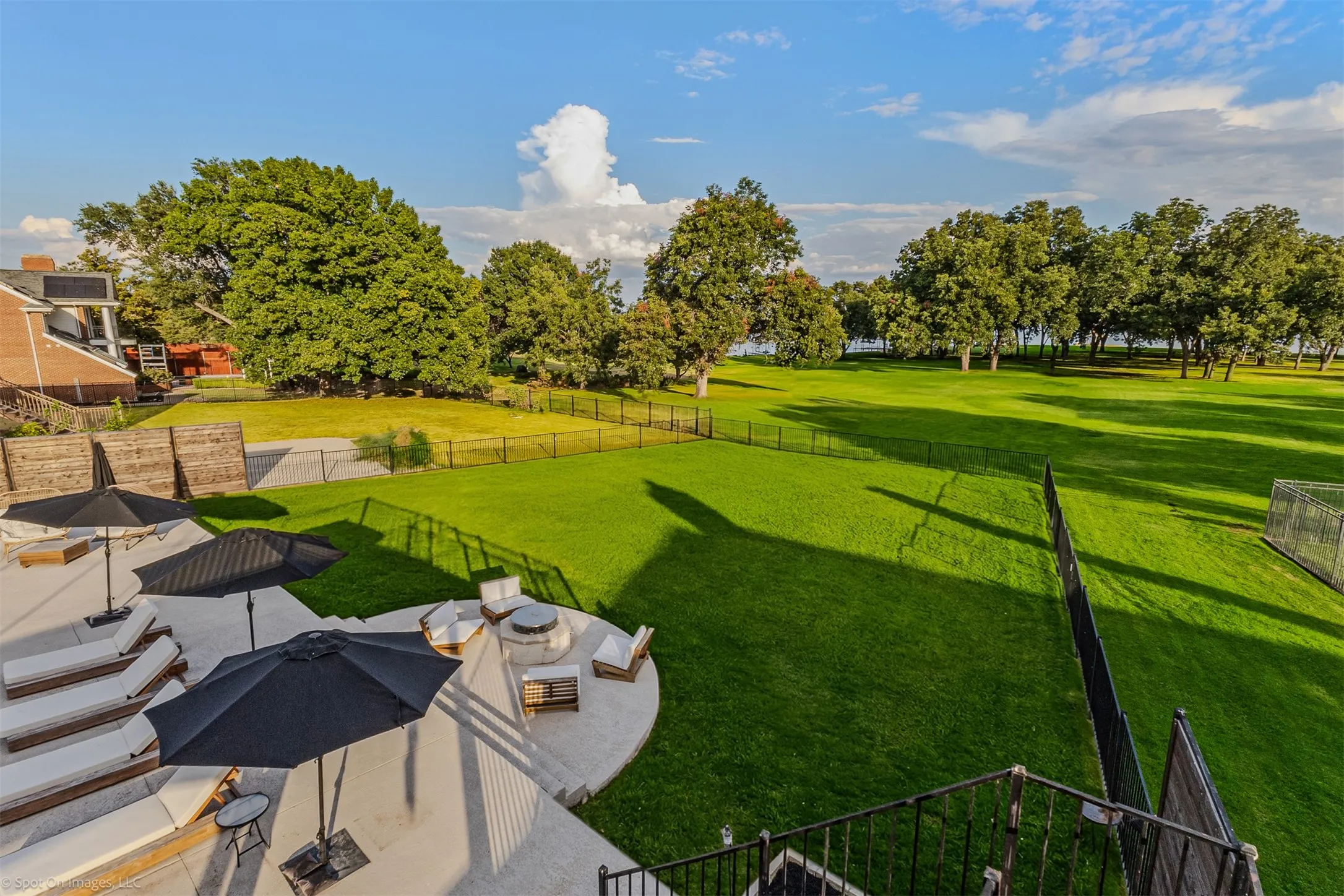 Expansive concrete patio with a built-in fire pit, surrounded by lush green lawn and mature trees