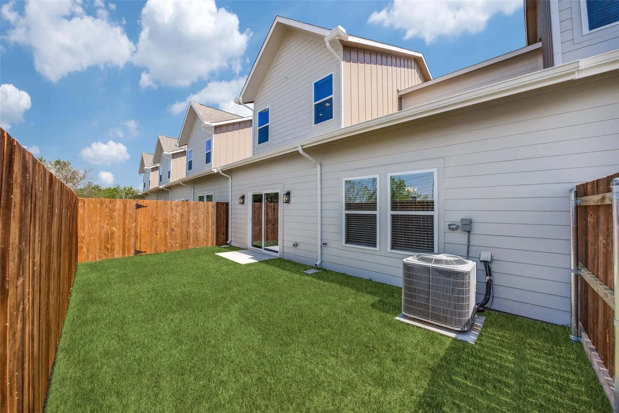 Private fenced yard with artificial turf, featuring a concrete patio and sliding glass doors