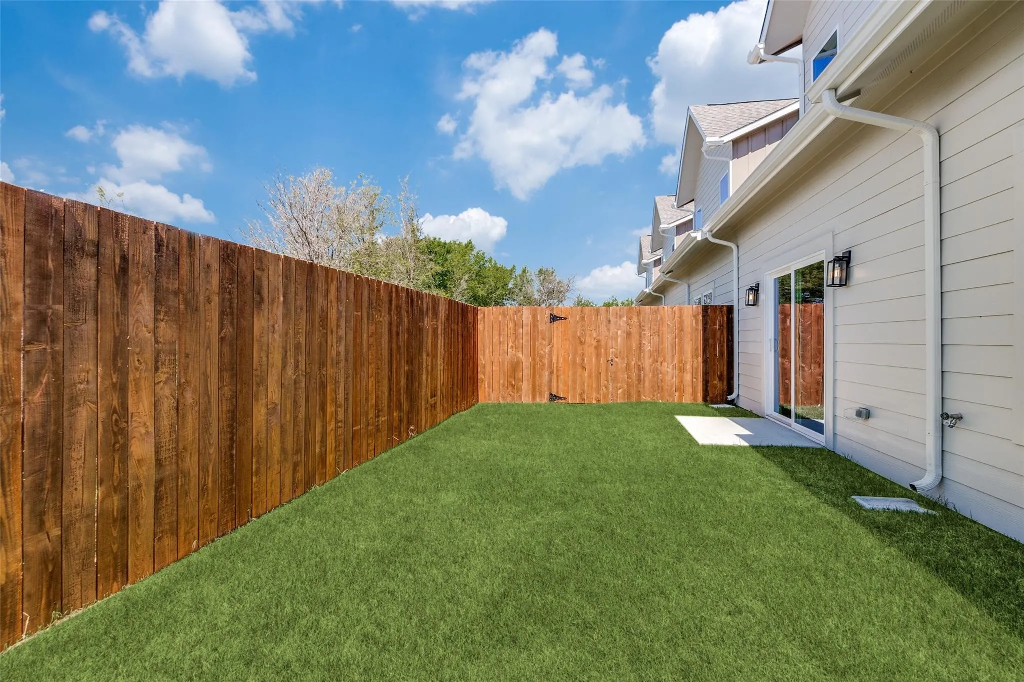 Private outdoor space featuring artificial turf, a wood fence, and exterior sconce lighting