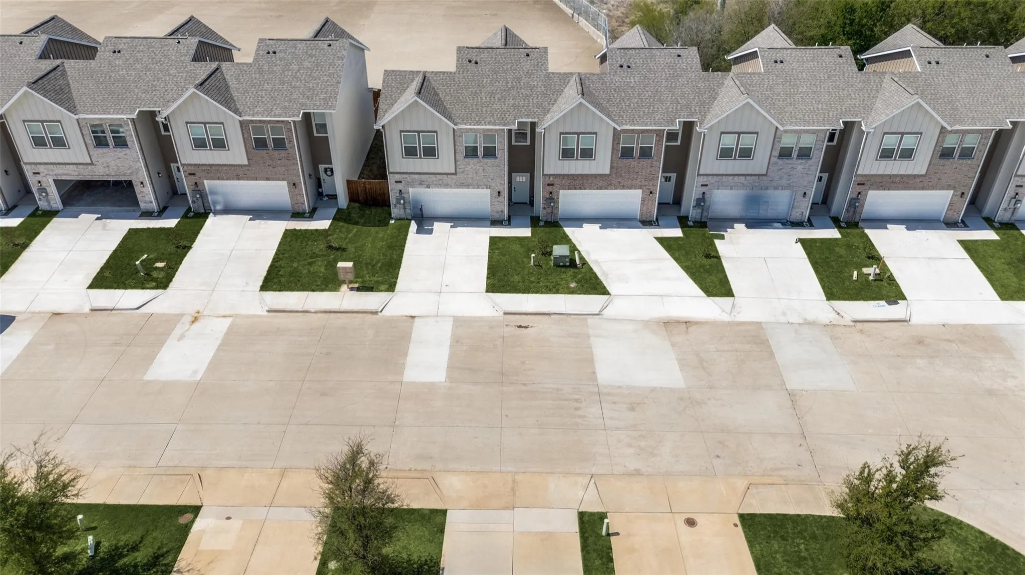 Row of modern townhomes featuring gabled roofs, brick and siding facades, attached garages, and concrete driveways