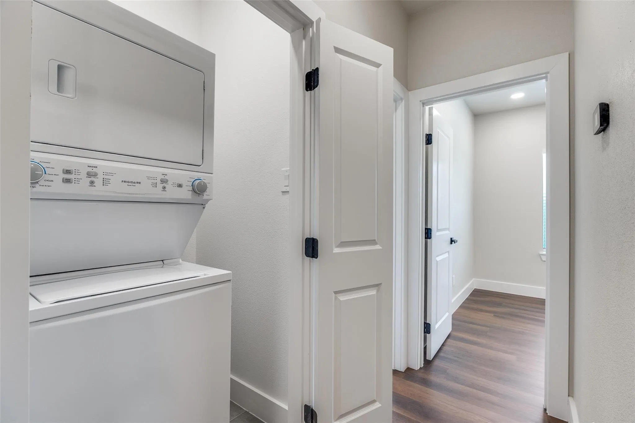 Stackable washer and dryer unit, white paneled doors, dark wood-finish flooring, and recessed lighting