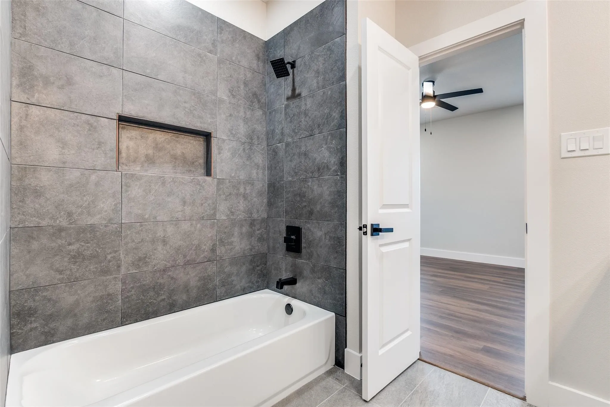 Bathtub and shower combination with large format wall tile, built-in shower niche, and matte black fixtures
