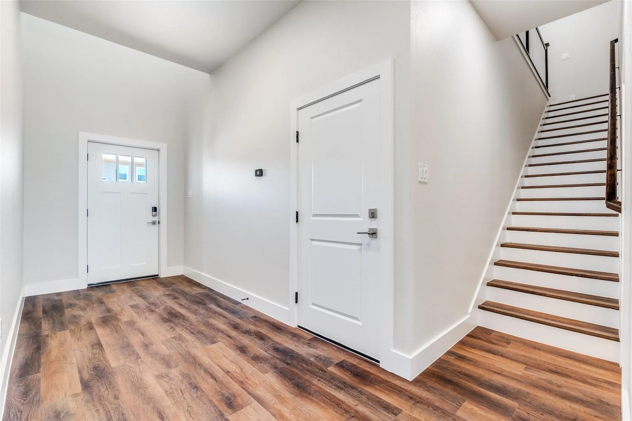 Entryway featuring wood-finish flooring, a contemporary white door with transom windows, and a staircase with wood treads and a modern railing