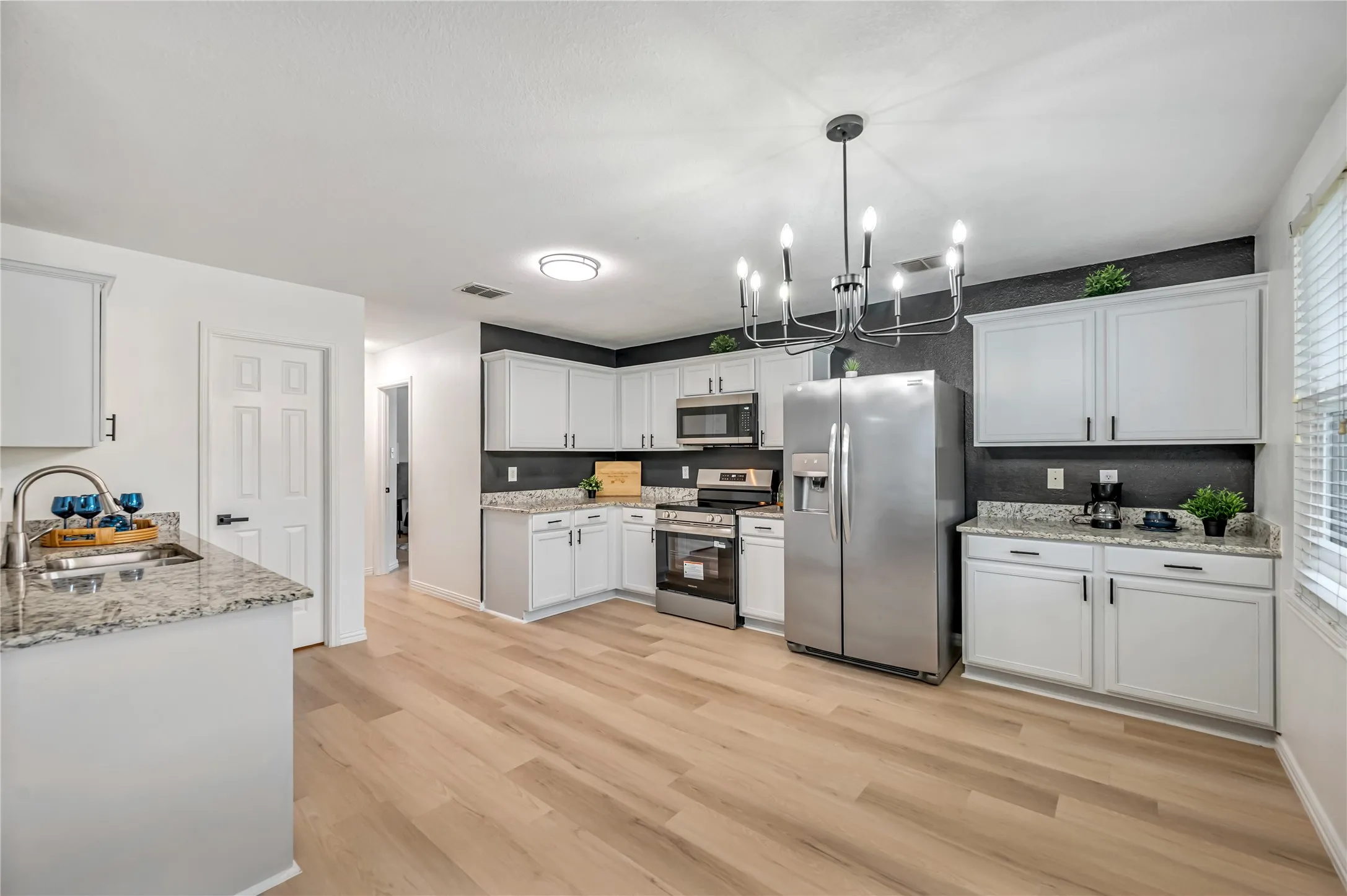 Kitchen featuring wood-finish flooring, white cabinetry, granite countertops, and stainless steel appliances