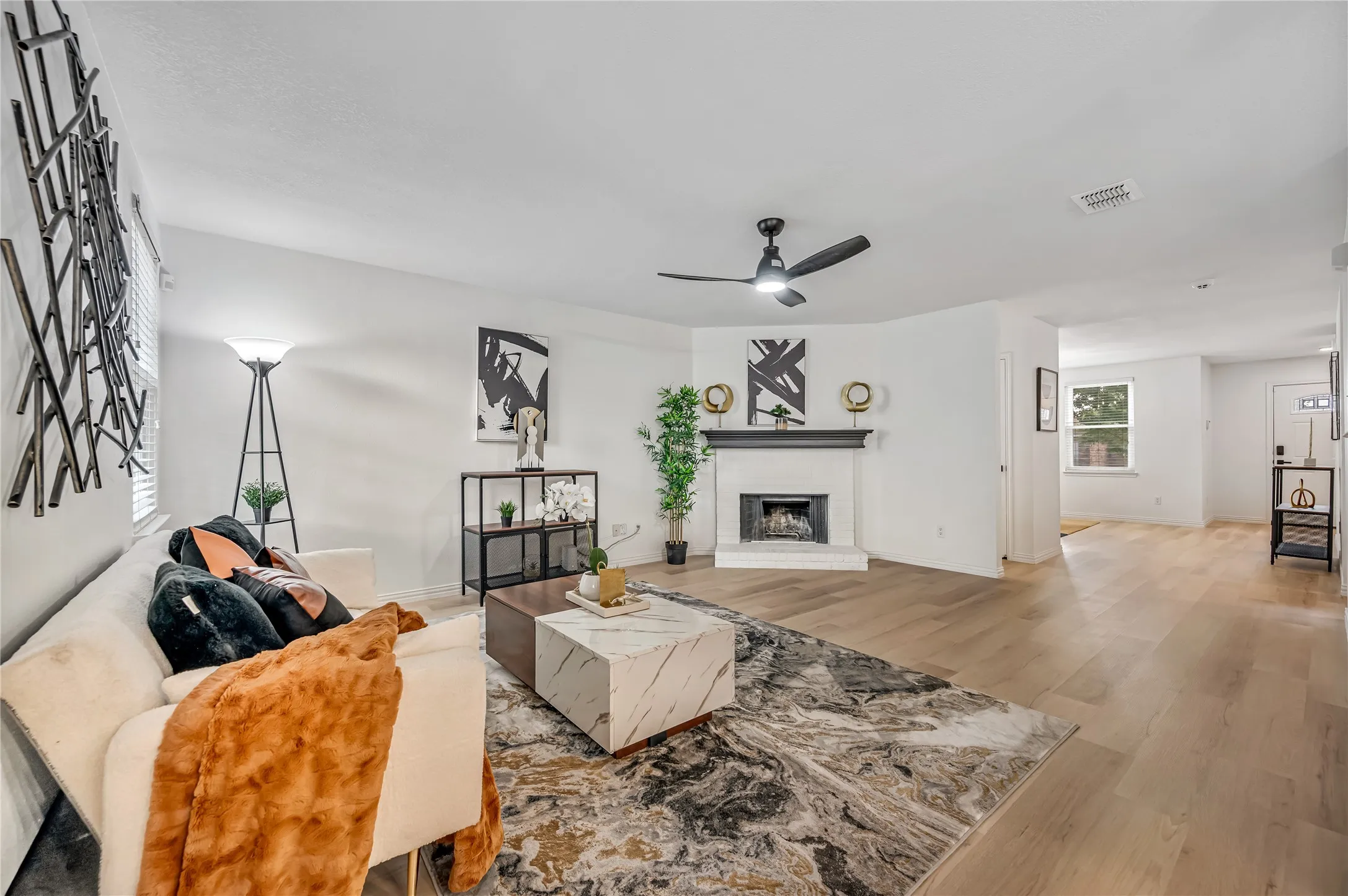 Expansive living area featuring light wood-finish flooring, a white brick fireplace with a dark mantle, and a ceiling fan