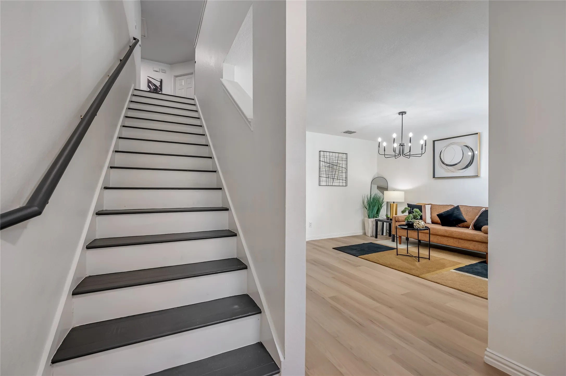 Modern light wood-finish flooring, a contemporary black chandelier, and a black handrail on a white staircase