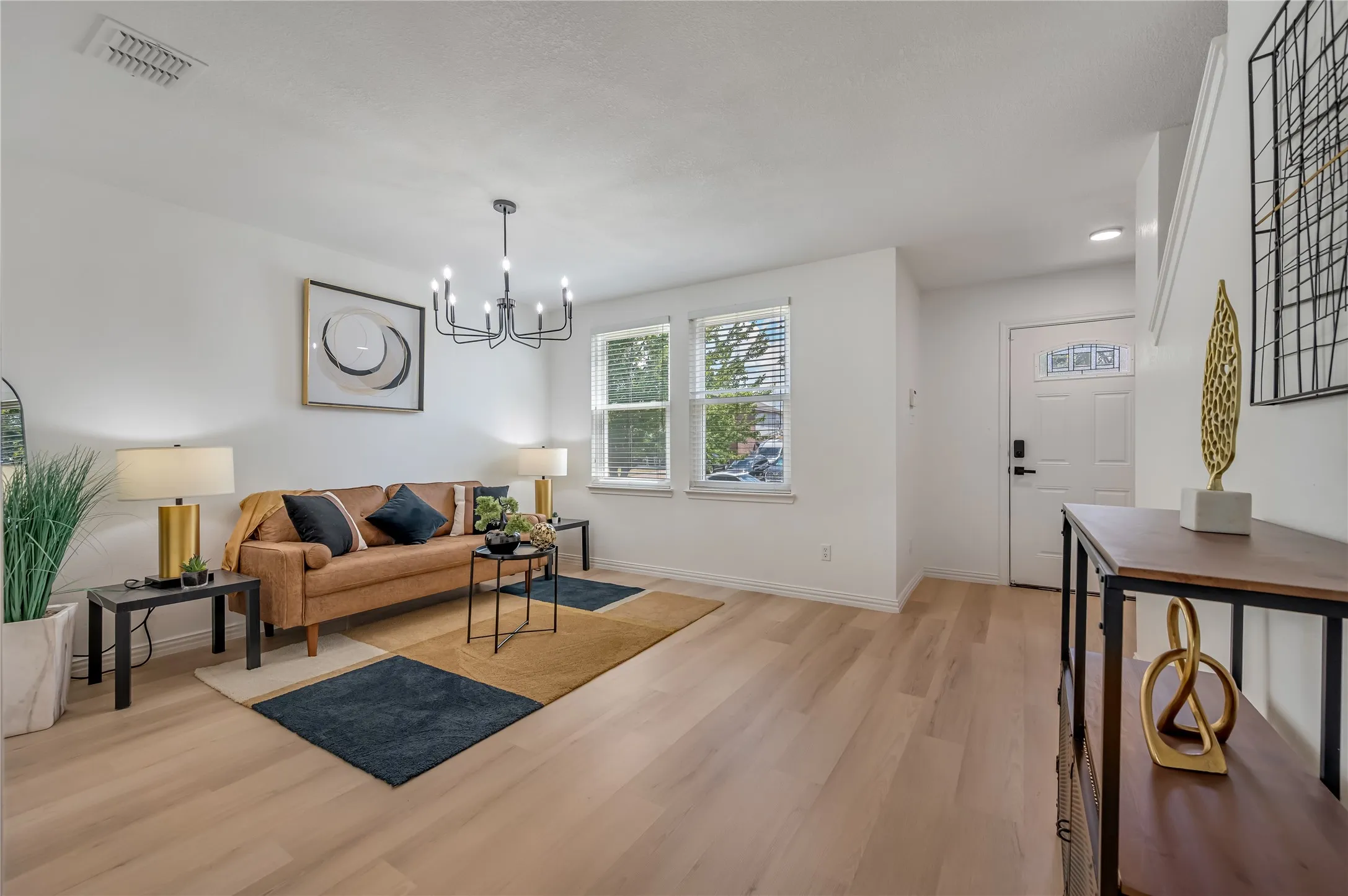 Light wood-finish flooring, white walls, and a black chandelier
